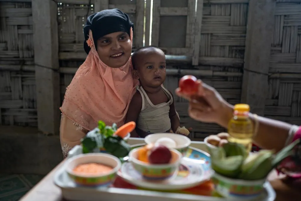 A woman and child sit at a table with bowls and plates of vegetables on it.