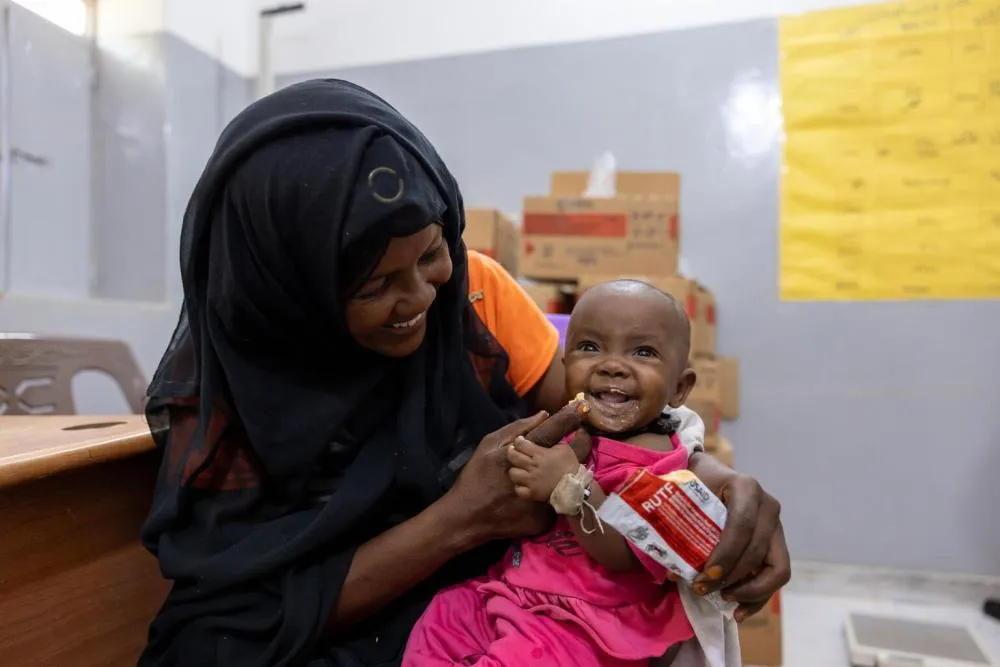 Une femme nourrit un bébé avec le contenu d’un sachet d’aliment thérapeutique prêt à l’emploi.