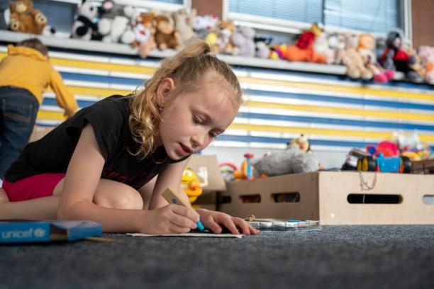Une fille assise par terre dessine avec une trousse récréative de l’UNICEF dans un centre adapté aux enfants.