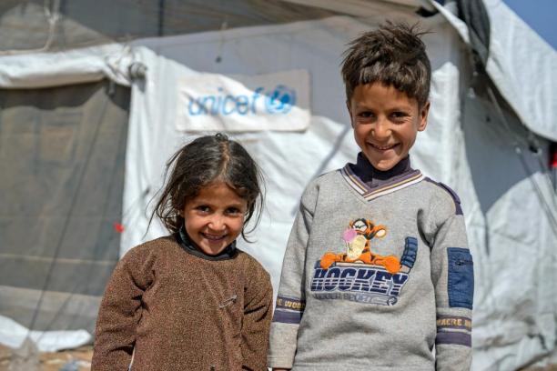 Deux enfants sourient devant une tente de l’UNICEF.