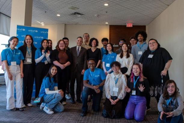 A group of 21 youth and adults smiling at the camera near a UNICEF Canada banner in an office setting.