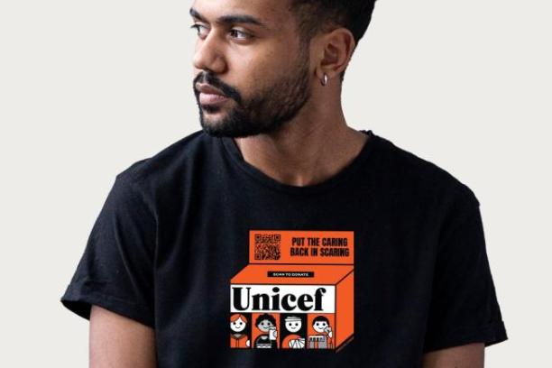 A person wearing the UNICEF X Kotn shirt with a vintage orange UNICEF box design on it.
