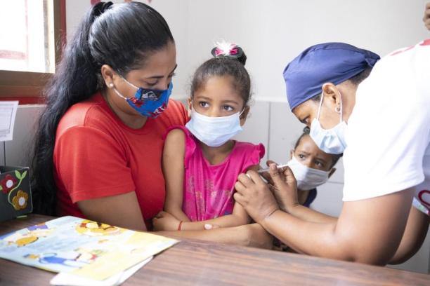 A child sitting beside her mother receives a vaccination from a health worker.