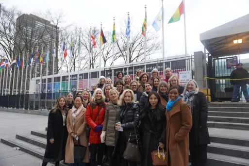 A group of women stand in front of a building with flags of different countries.