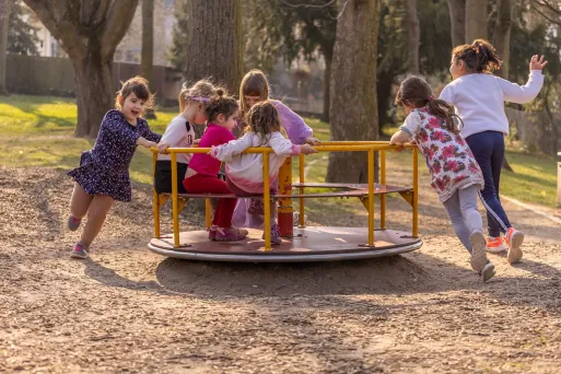 A group of children playing on a merry go round in the playground.