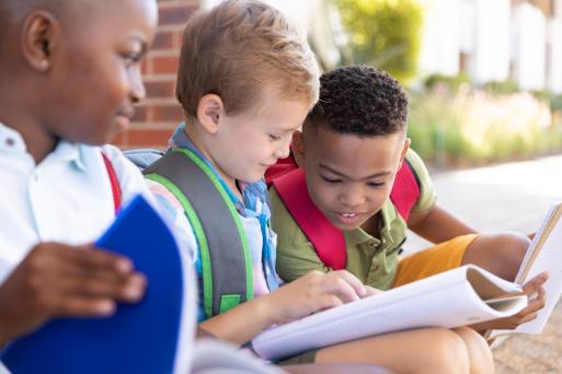 A group of boys are sitting outdoors and looking at a book together. 