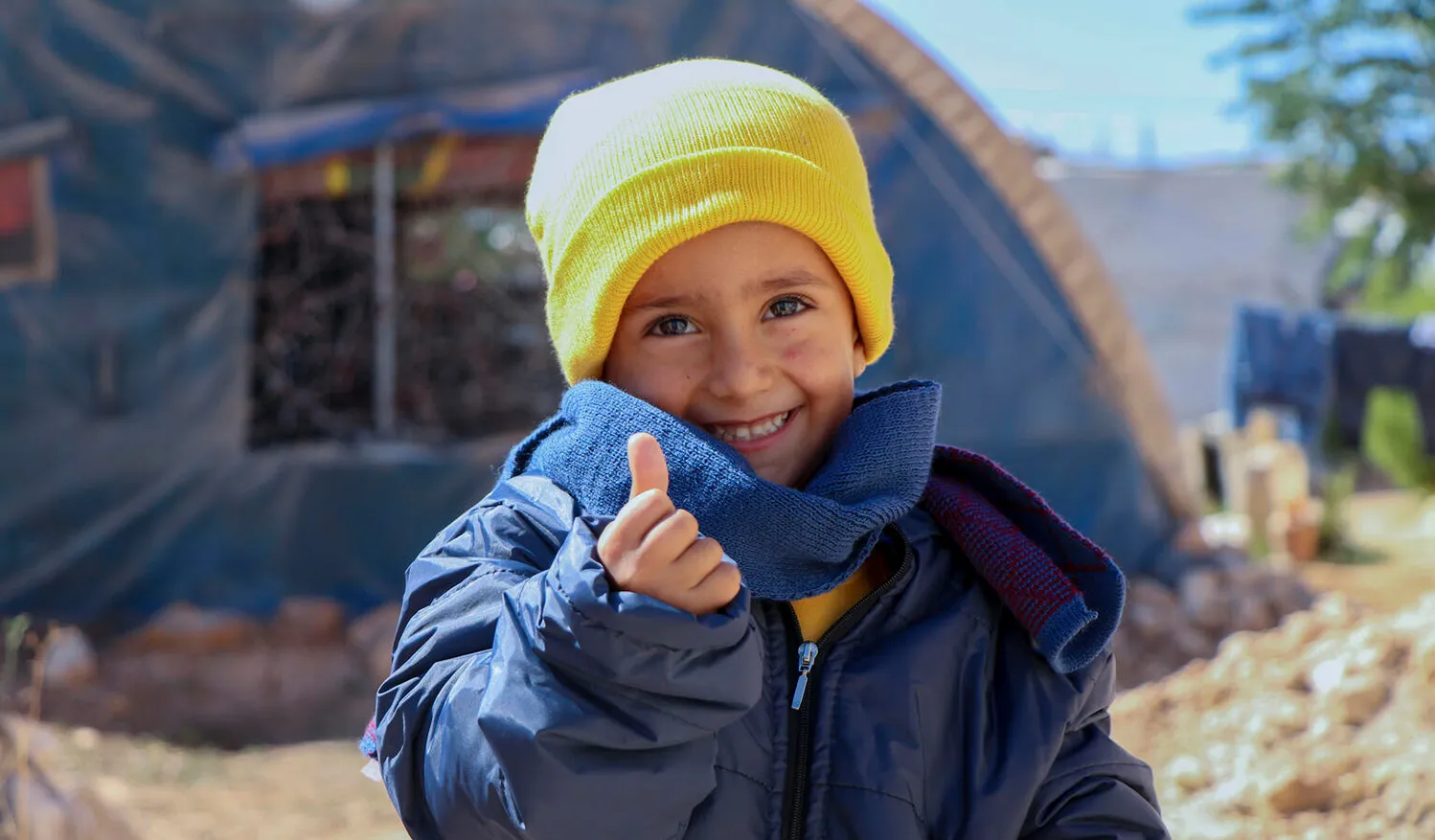 In Syria, 4-year-old Rashid smiles and gives a thumbs-up sign, while wearing his new winter clothes distributed by UNICEF in Fafin camp for displaced families.