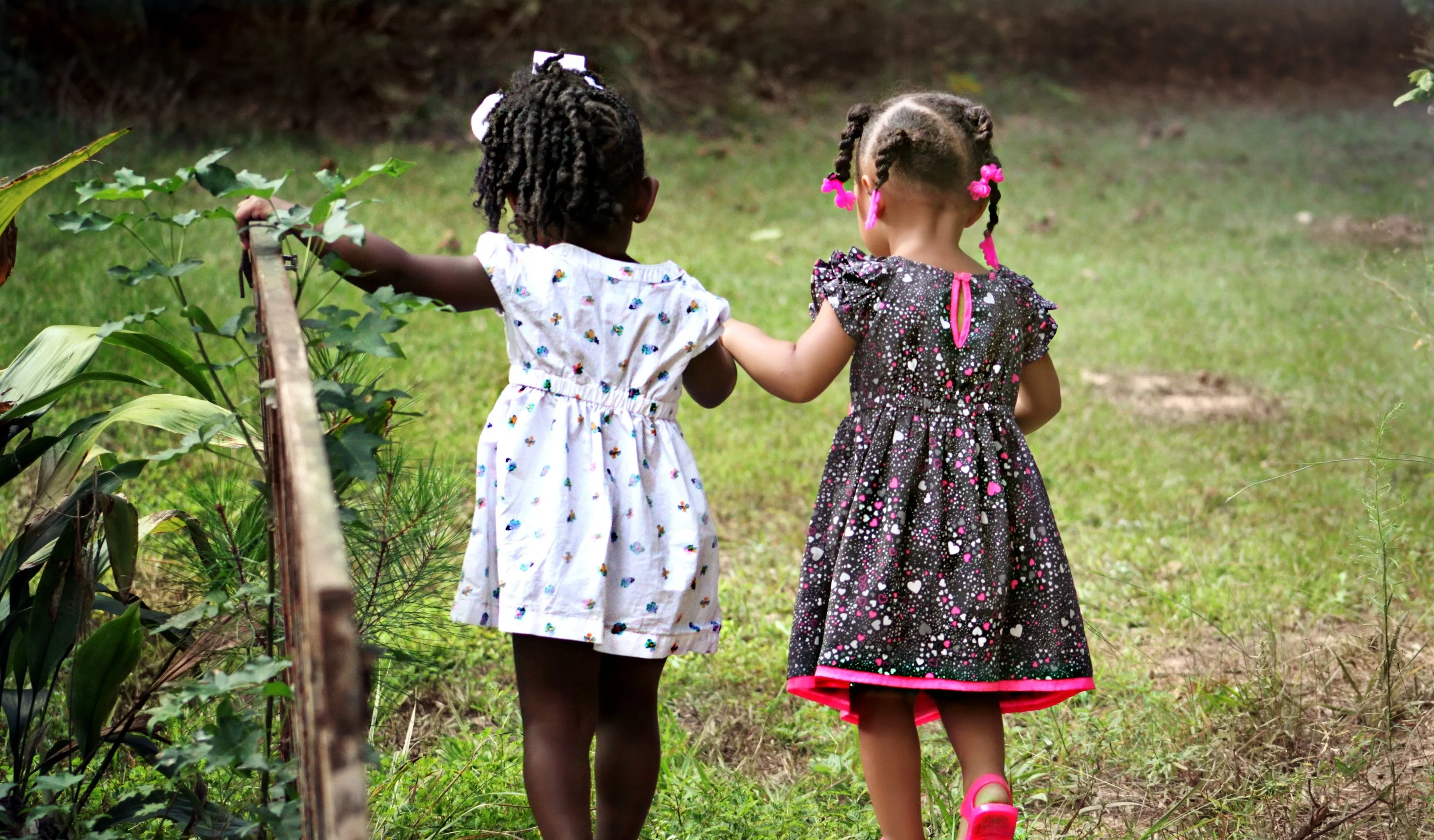 Two girls, holding hands, walk across a bridge.