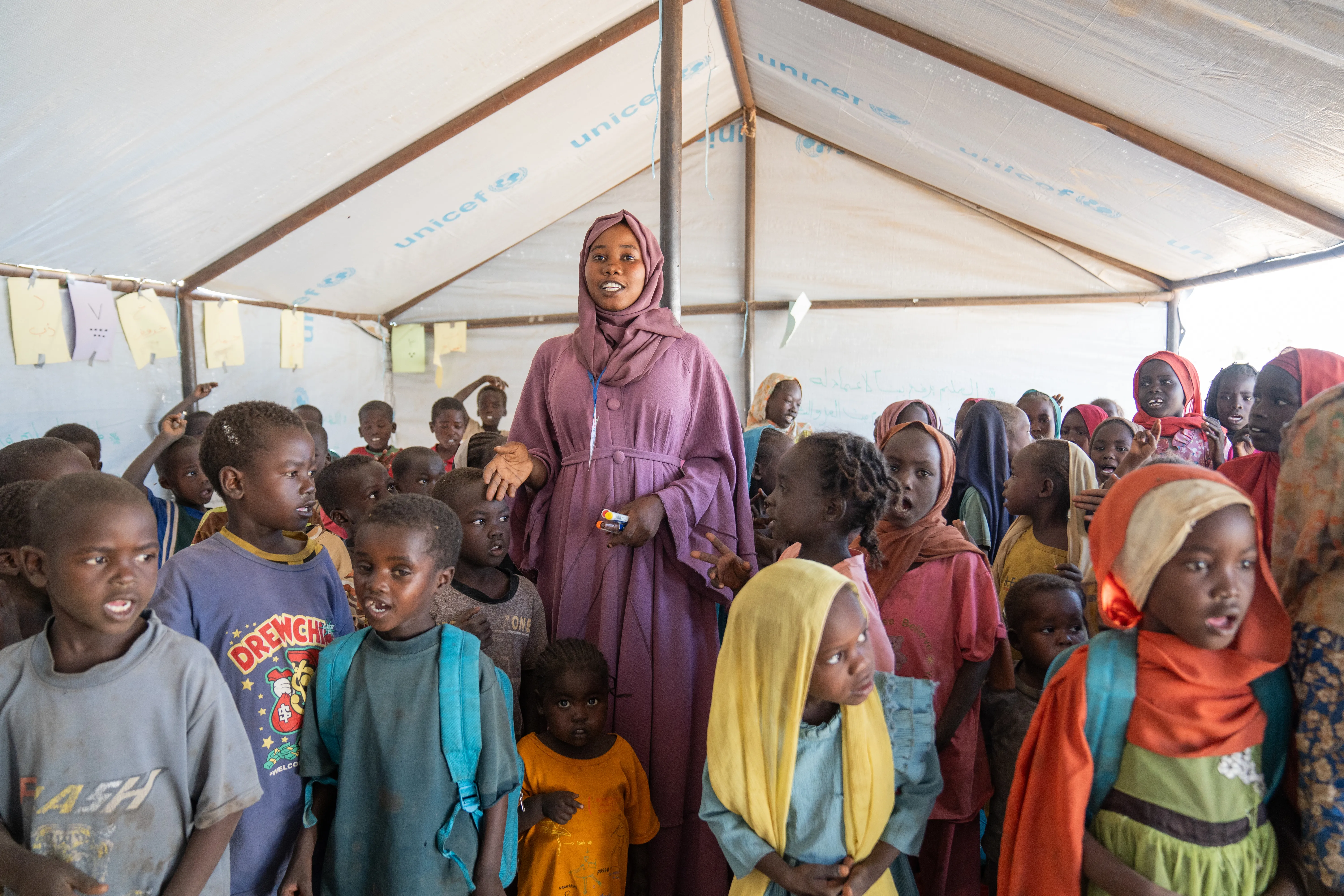 Une femme vêtue de violet se tient au milieu d’un groupe d’enfants dans une tente.