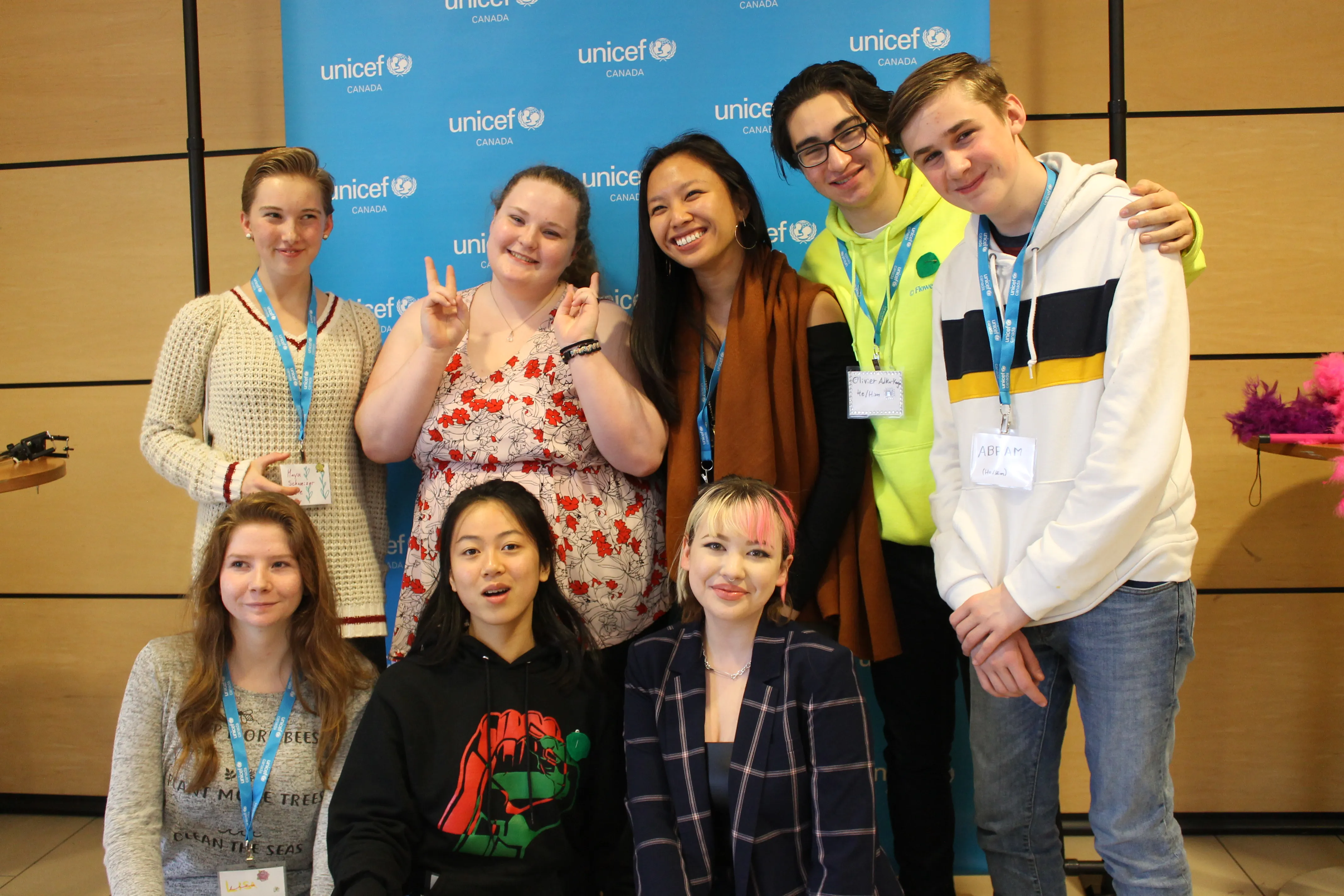 Eight children stand in front of a UNICEF Canada sign, they are all wearing UNICEF lanyards. This photo was taken in Toronto, Canada in 2019. 
