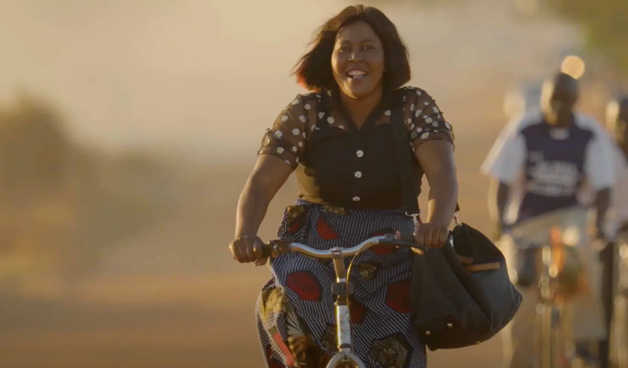 A woman with a book bag rides a bicycle down a street 