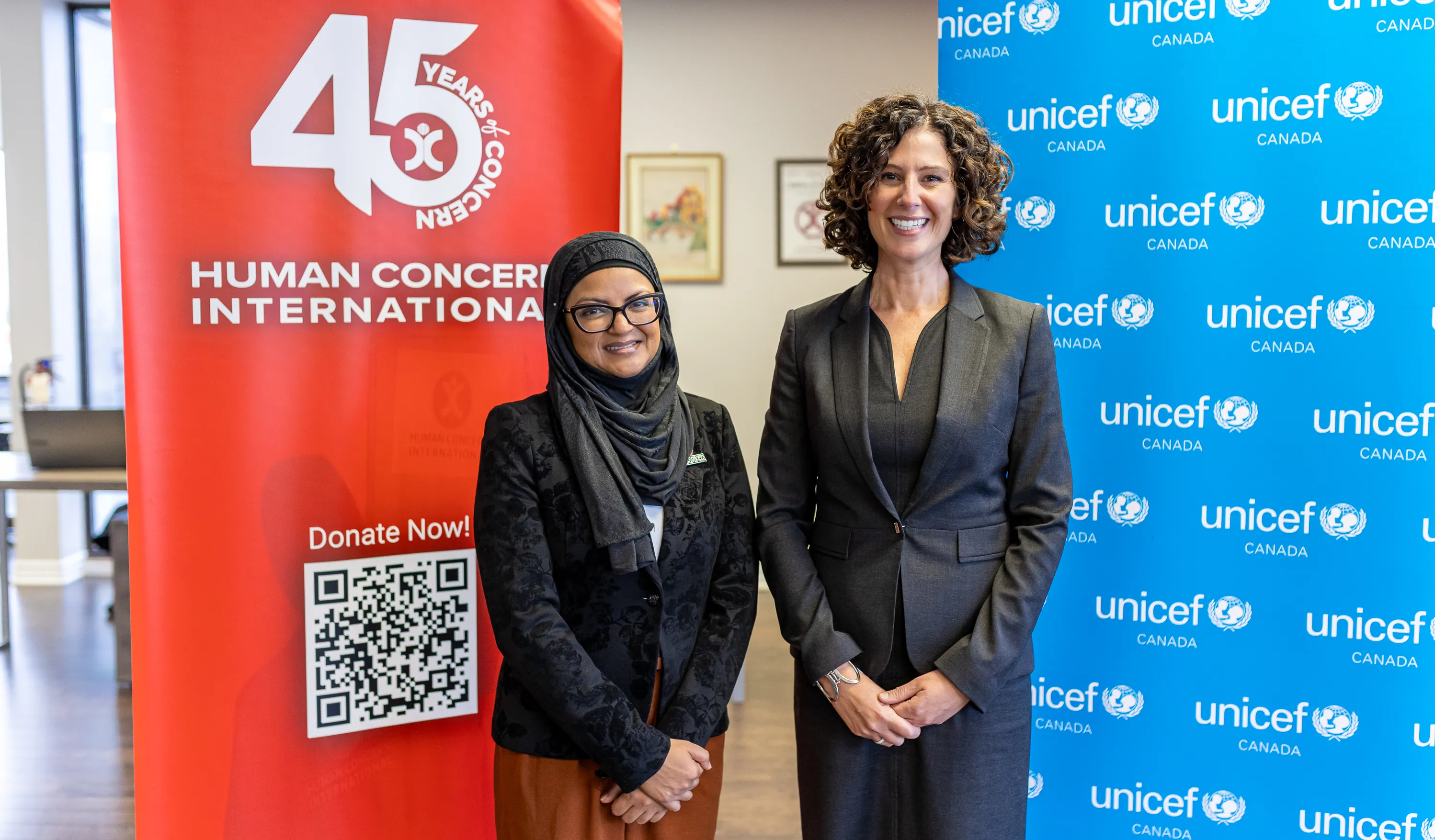 Mahmuda Khan, CEO of Human Concern International and Sevaun Palvetzian, President and CEO of UNICEF Canada pose for a photo in front of HCI and UNICEF Canada banners.