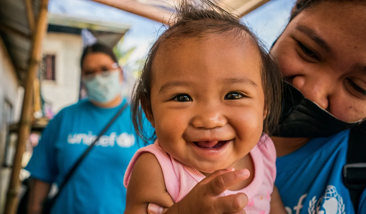 Close-up of a smiling toddler girl as she is held by a UNICEF worker, Philippines.