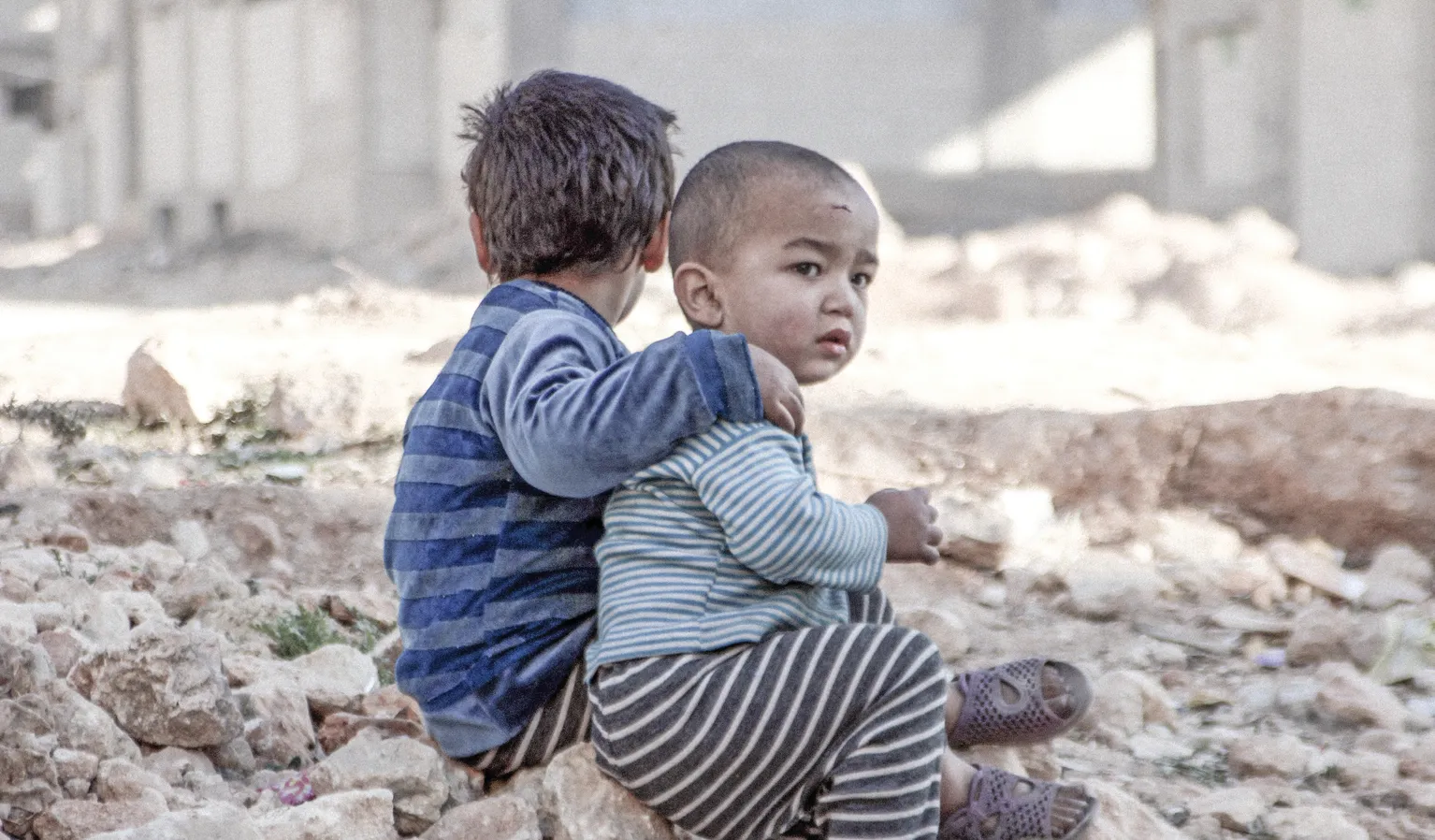Two children sit in the rubble of their former home.