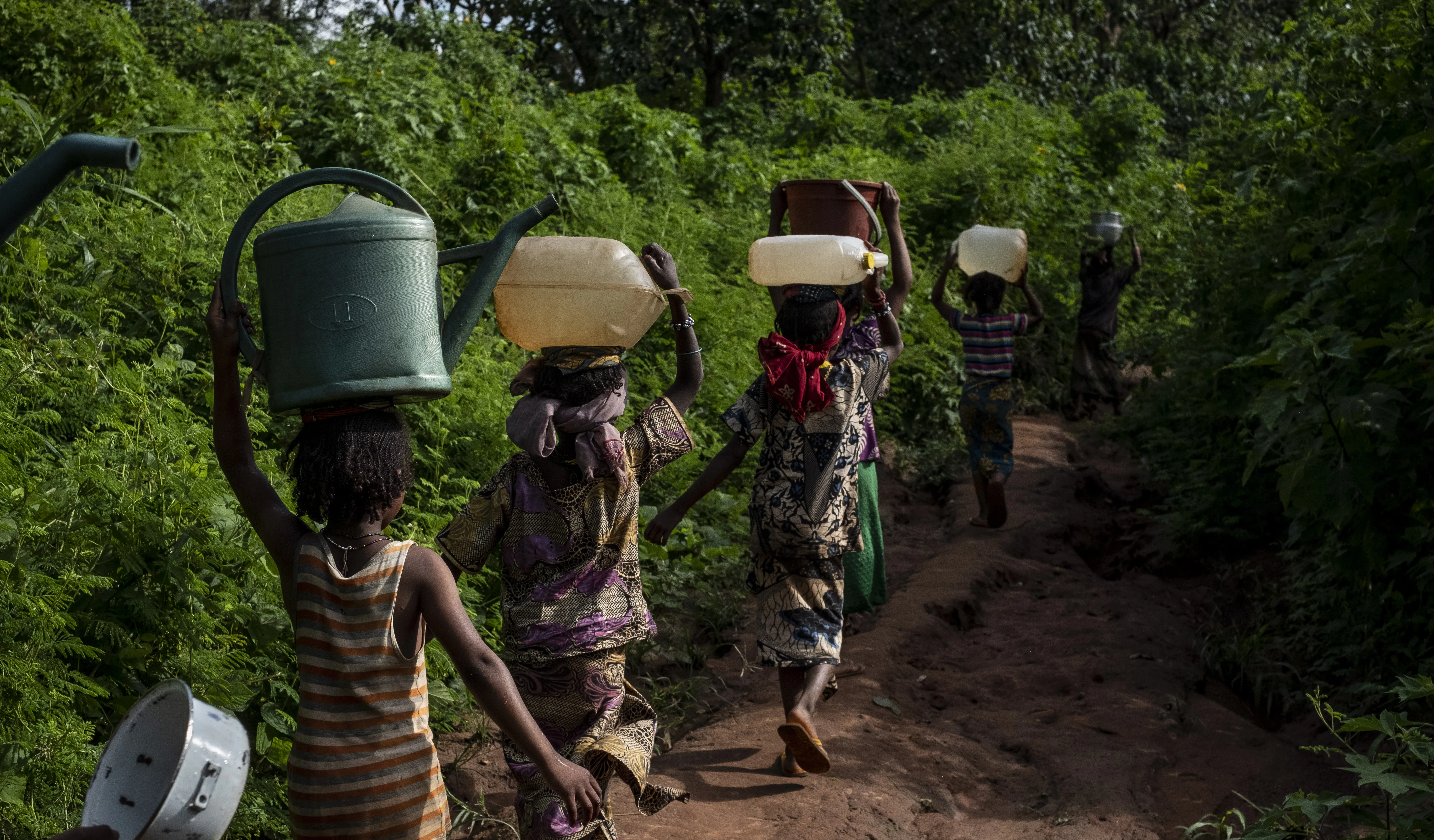 Des enfants marchent sur un chemin dans la forêt, portant des seaux sur la tête, pour puiser de l'eau d'une source naturelle au camp d'Elevage à Bambari, en République centrafricaine