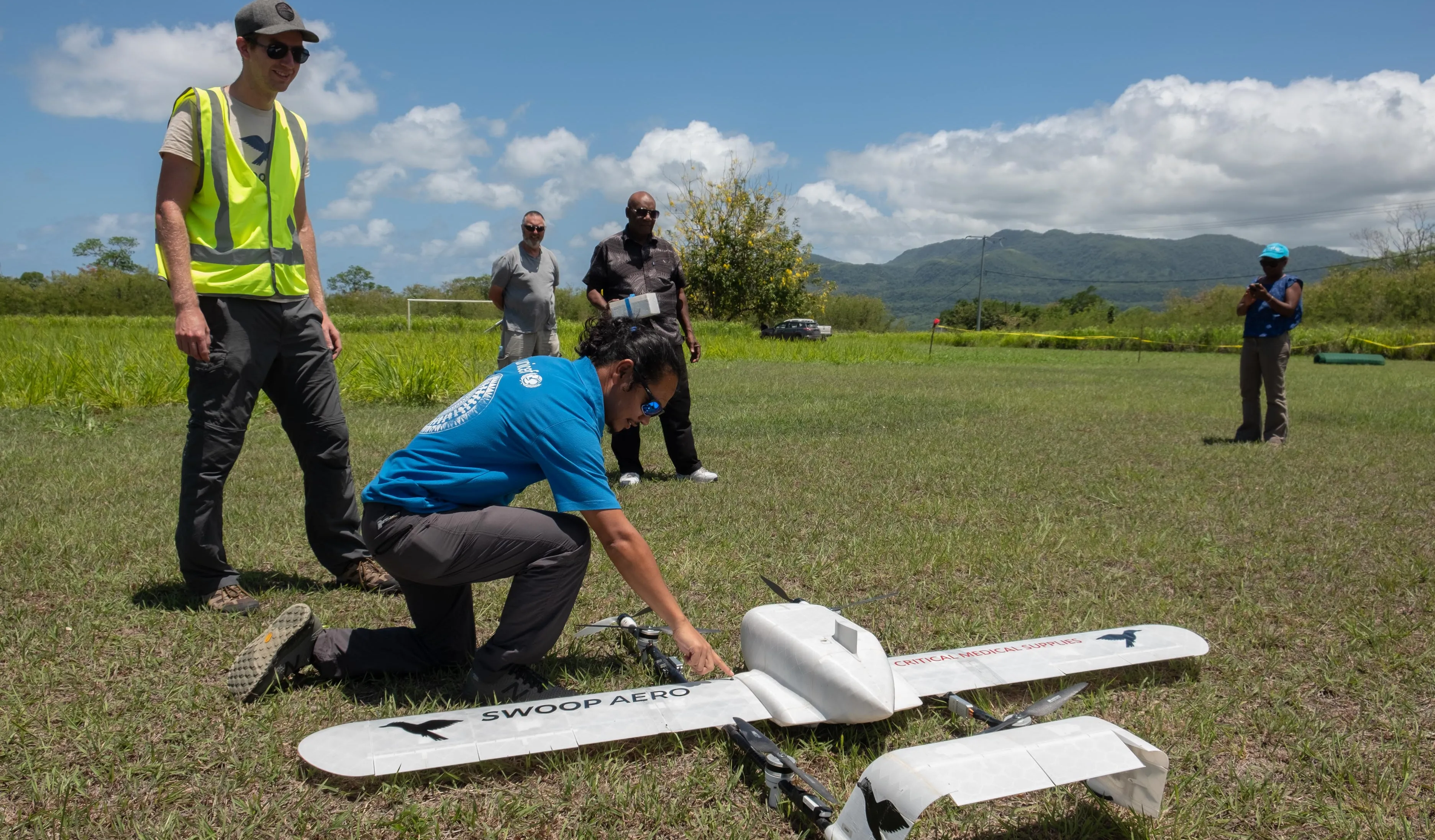 A man in a UNICEF t-shirt bends down to check on a small white drone in a field in Vanuatu. 
