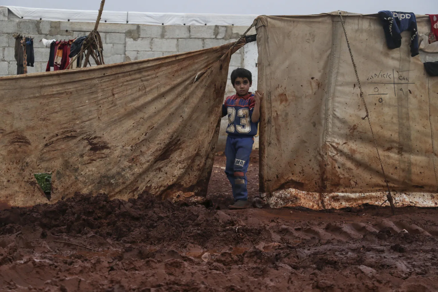 Young boy stands near the tent where he lives with his family, Atma camp, Idlib