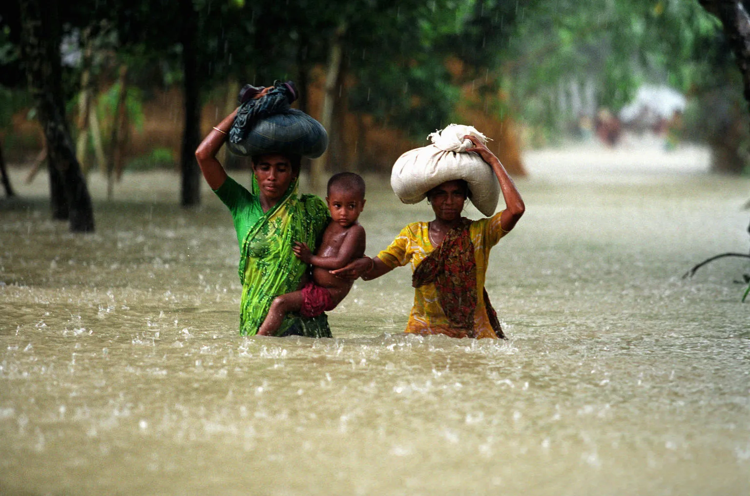 Two women and a small child wade through floodwaters in Bangladesh.