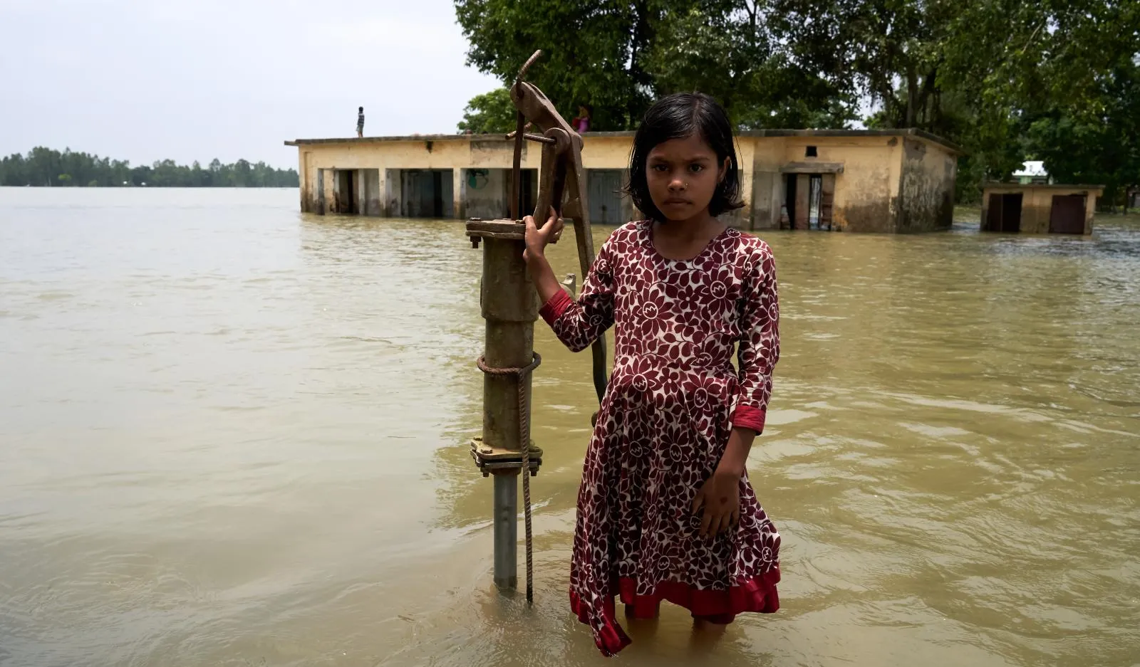A little girl stands near a flooded water pump in India.