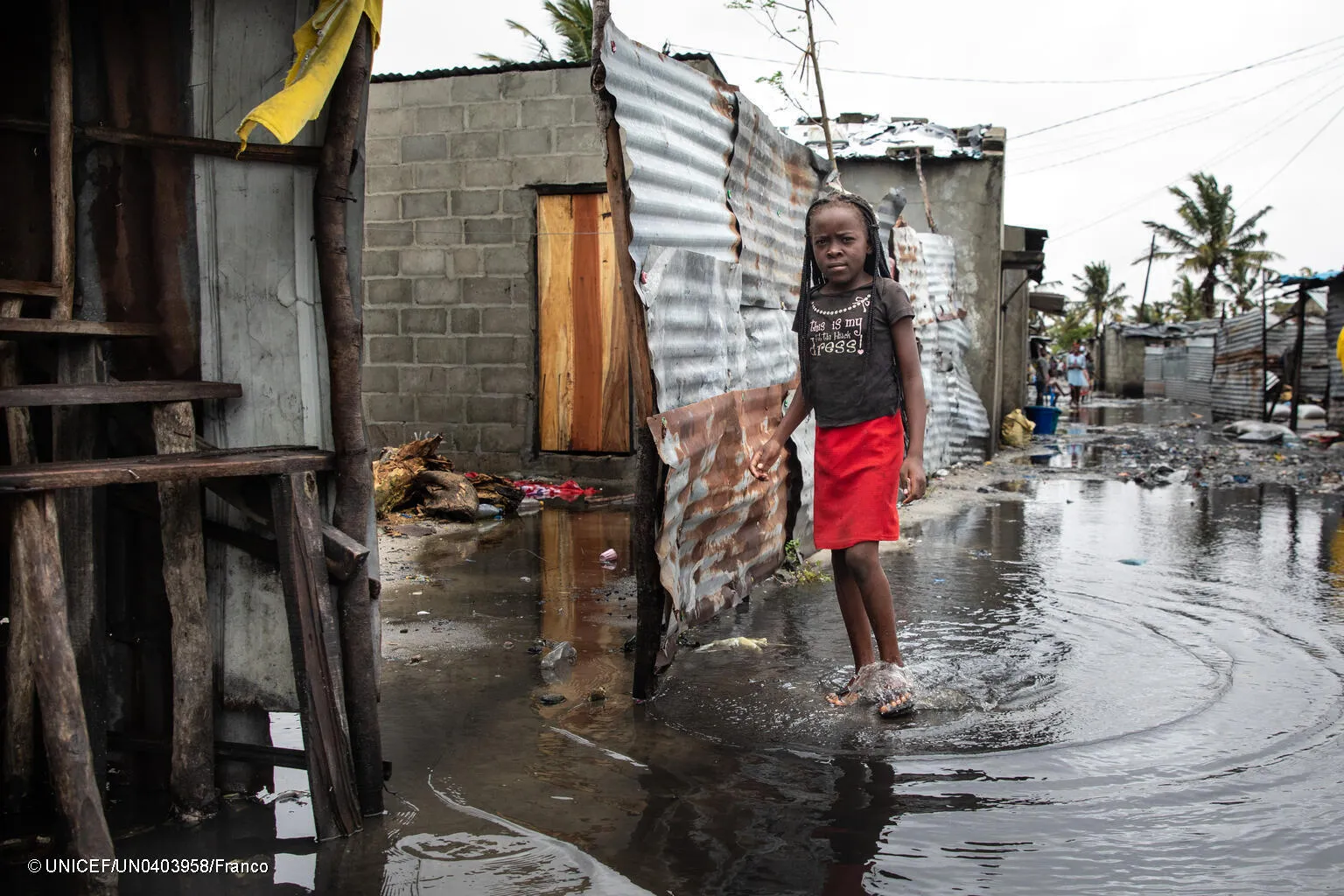 A girl walks through an inundated street in a slum-like setting, with the walls of some homes destroyed. This photo was taken in Mozambique. 