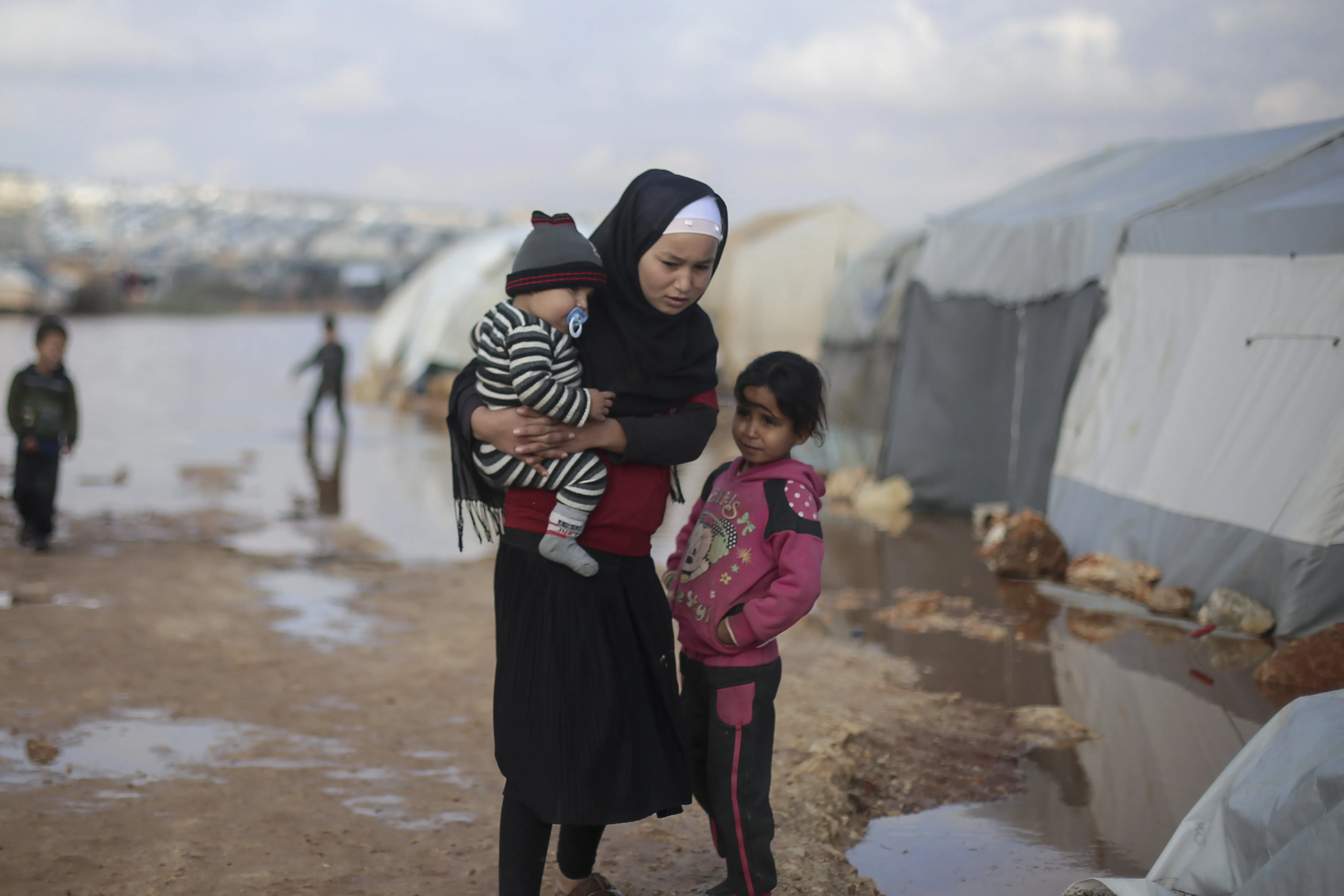On 19 January 2021, families stand outside of tents in a flooded area of Kafr Losin Camp in northwest Syrian Arab Republic.