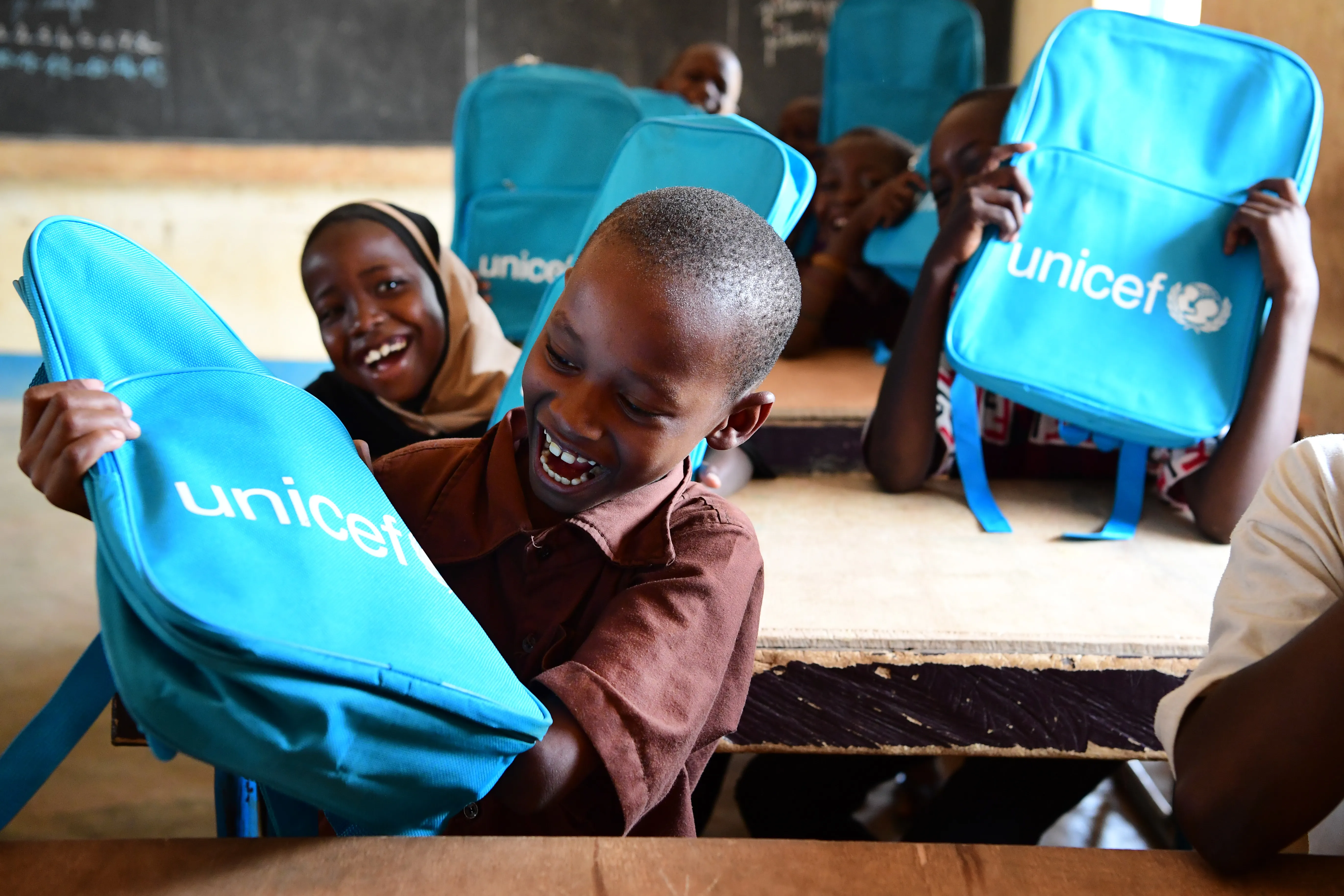 Au Niger, des élèves enthousiastes sourient et rient à leur pupitre après avoir reçu des sacs à dos de l’UNICEF remplis de fournitures scolaires.