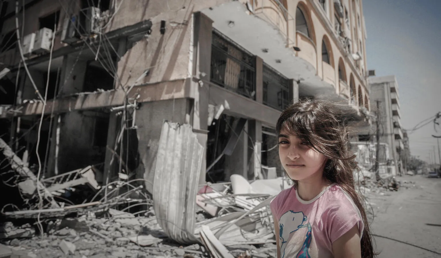 On 17 May 2021, a Palestinian girl stands in front of their home as her family extracts their possessions from inside their damaged home after being targeted in Gaza City.