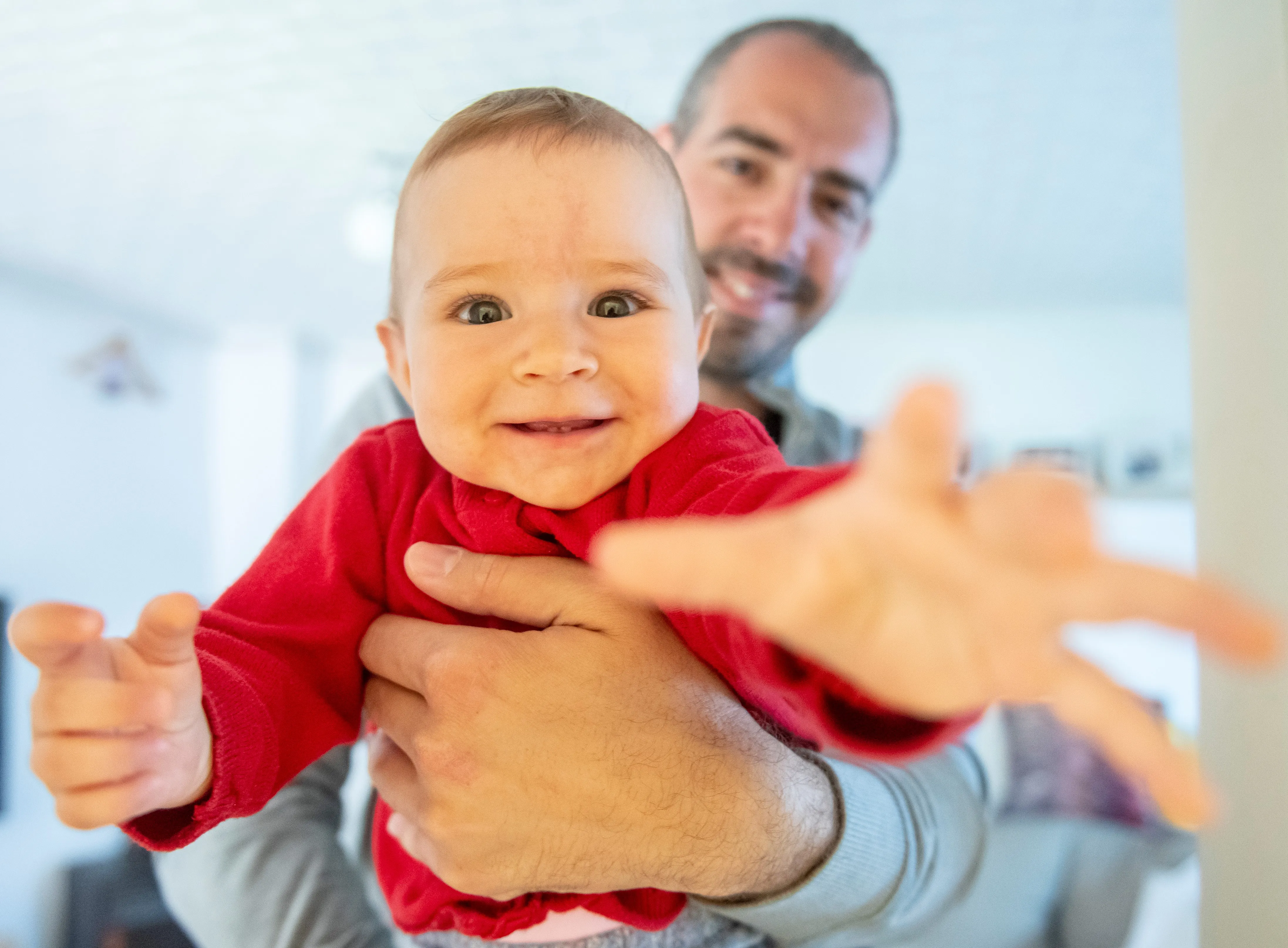 Toddler being held by his father reaches for the camera