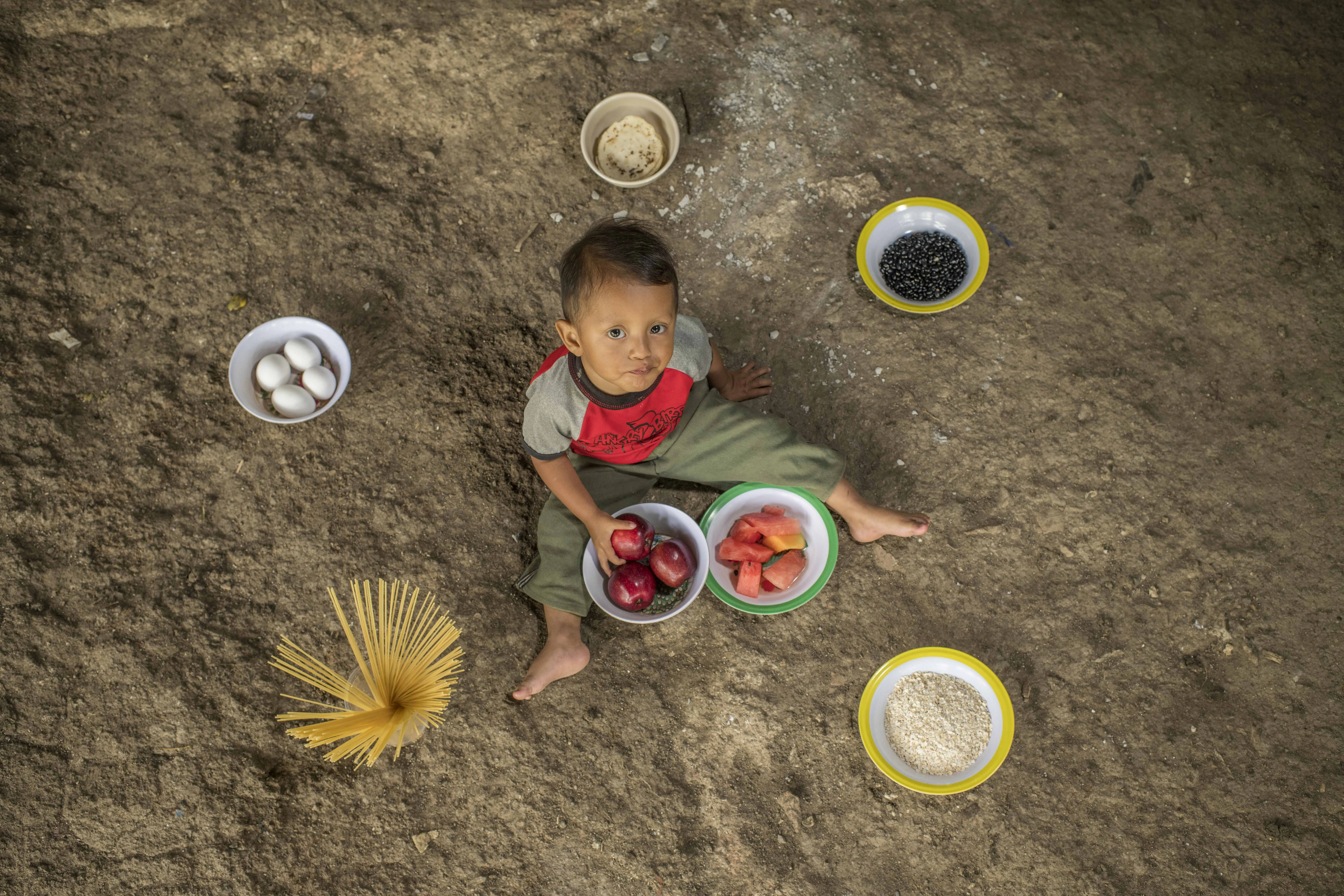 Hender Jonathan Godínez Hernandez, 23 months old, eats an apple and poses on the floor of the patio of her house. In the dishes there are beans, tortillas, rice, tomatoes, eggs, pasta and fruits. These foods are what his mother usually includes in his diet.