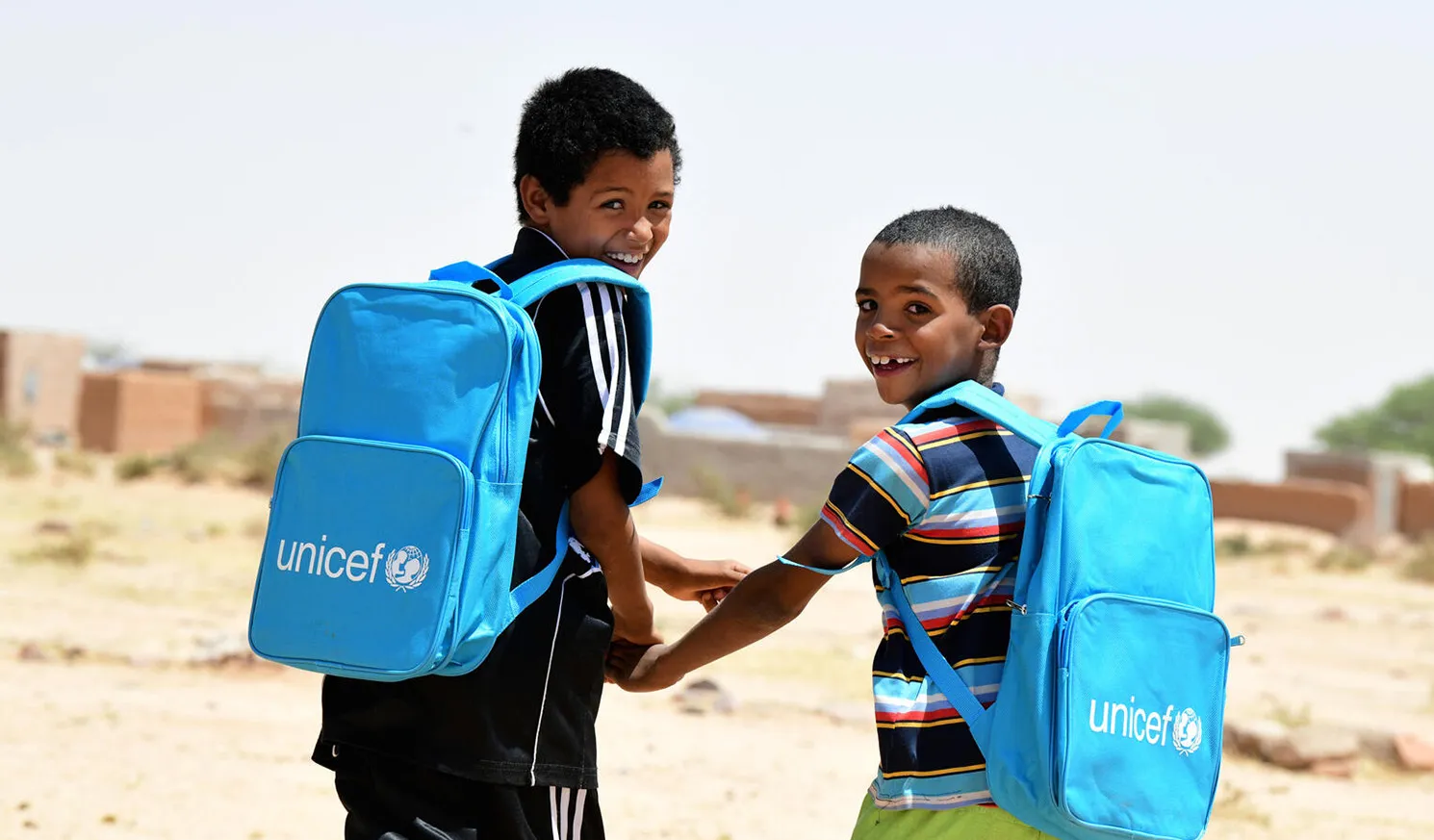 Dans le nord du Niger, deux enfants rient et marchent ensemble en portant leurs nouveaux sacs à dos de l’UNICEF remplis de fournitures scolaires.