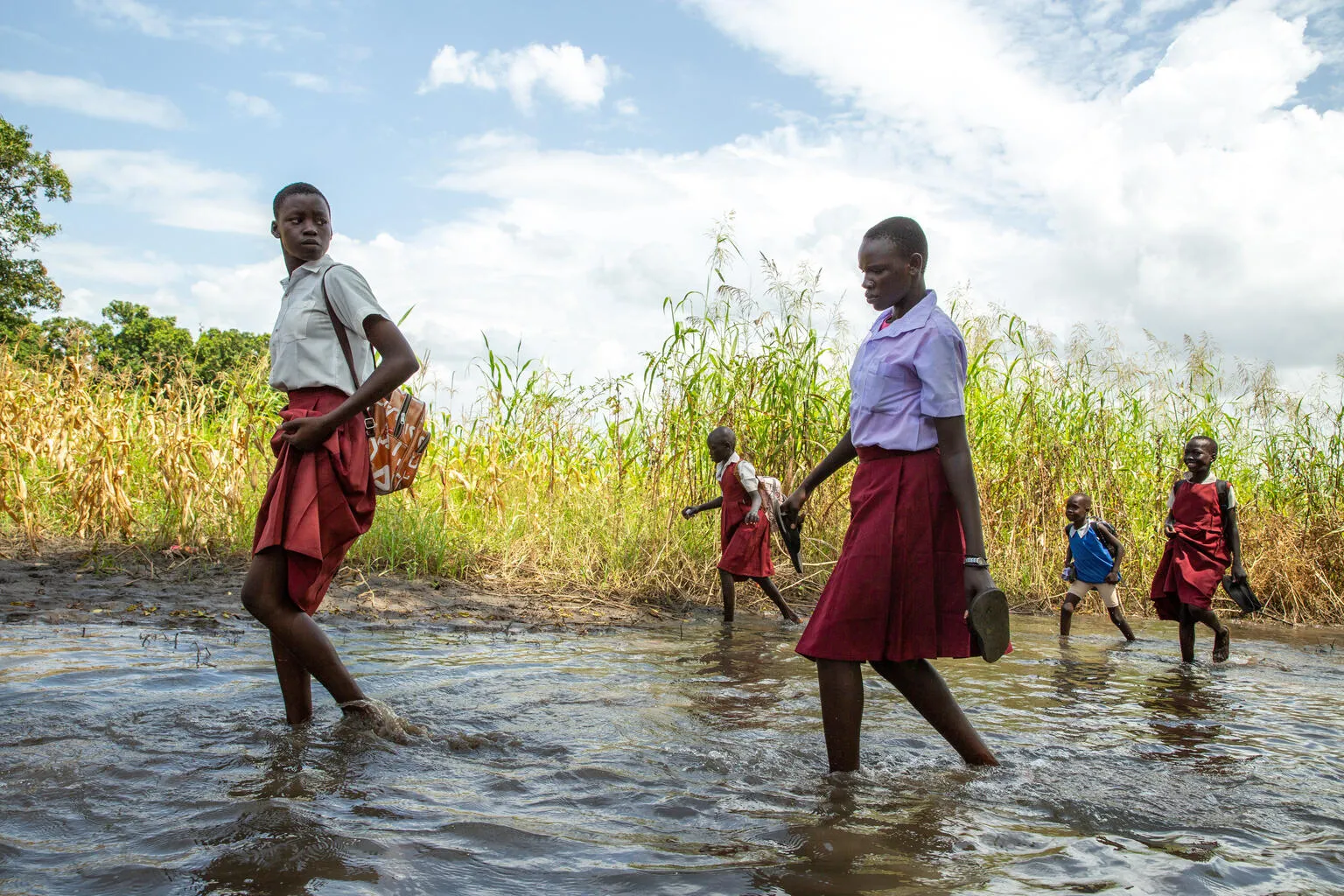 Students walking on foot across flooded paths - South Sudan