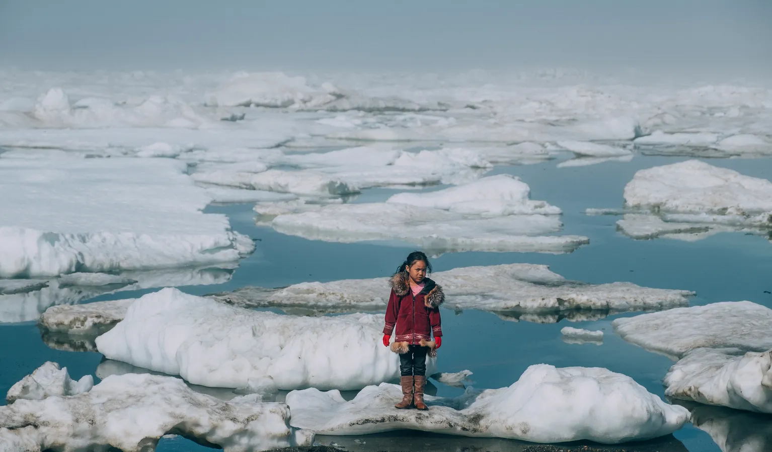 Alaska, United States: a girl wearing a red coat stands on an ice floe.