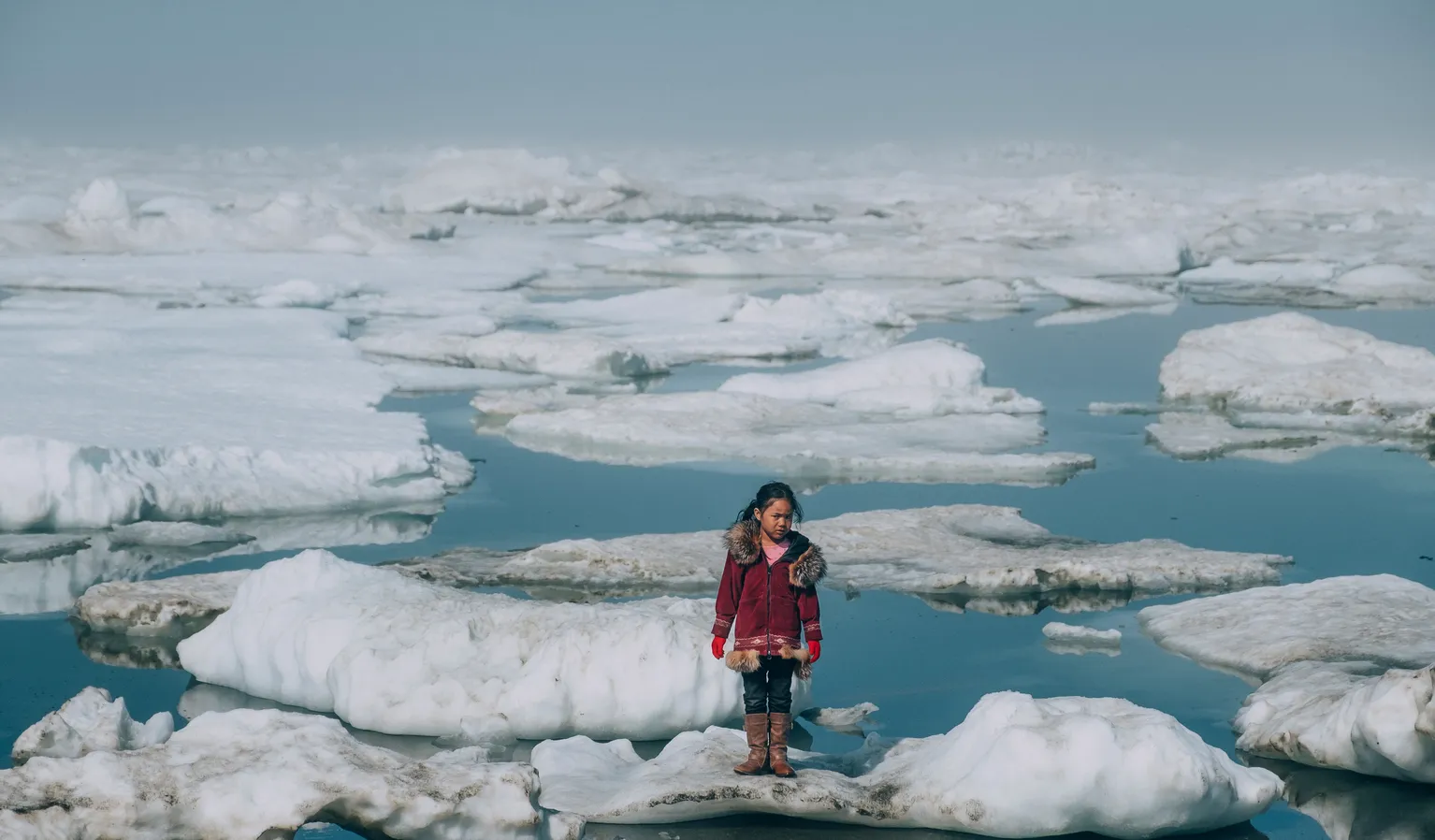 Alaska, United States: a girl wearing a red coat stands on an ice floe