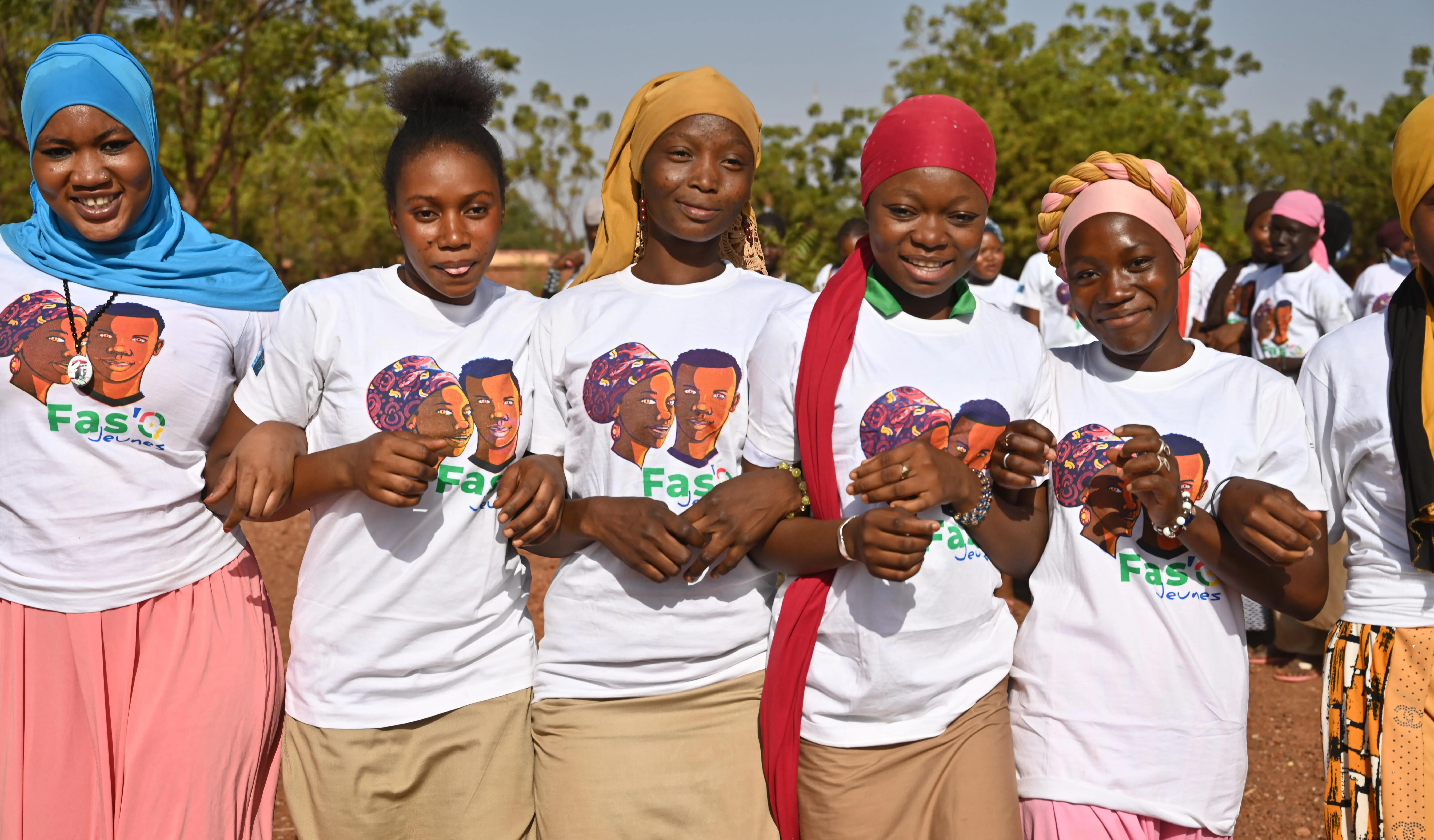 Five women face the camera, smiling, whilst interlocking their arms.