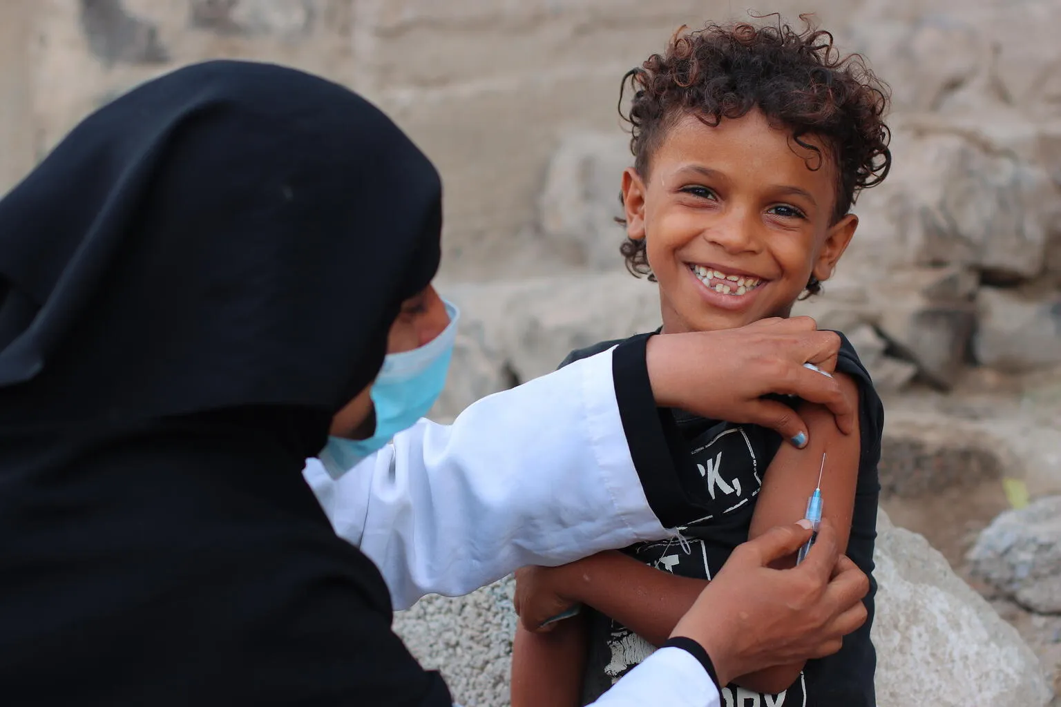 Young child smiling at camera while getting vaccinated in Yemen.