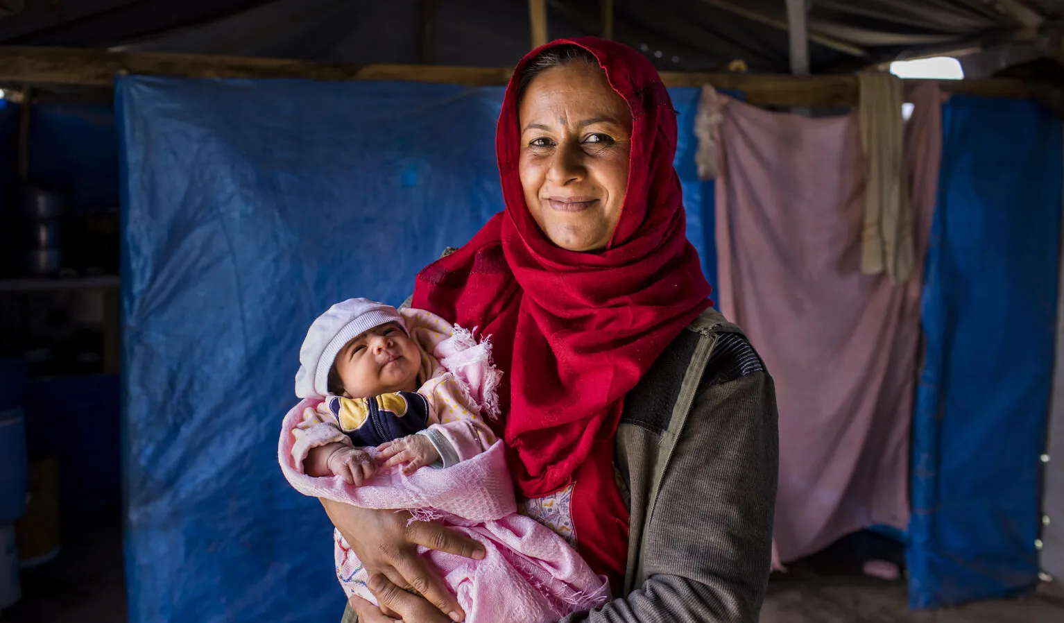 A mother in front of tent holding a new born in a pink blanket.