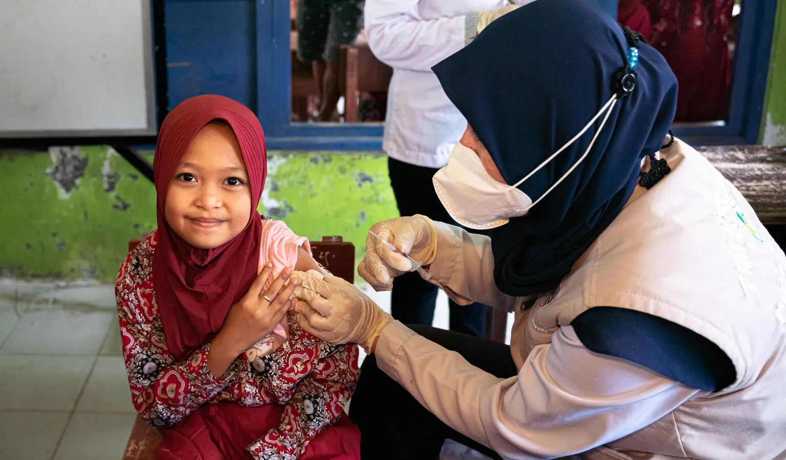 A girl looks at the camera as a nurse administrators an injection to her arm. 