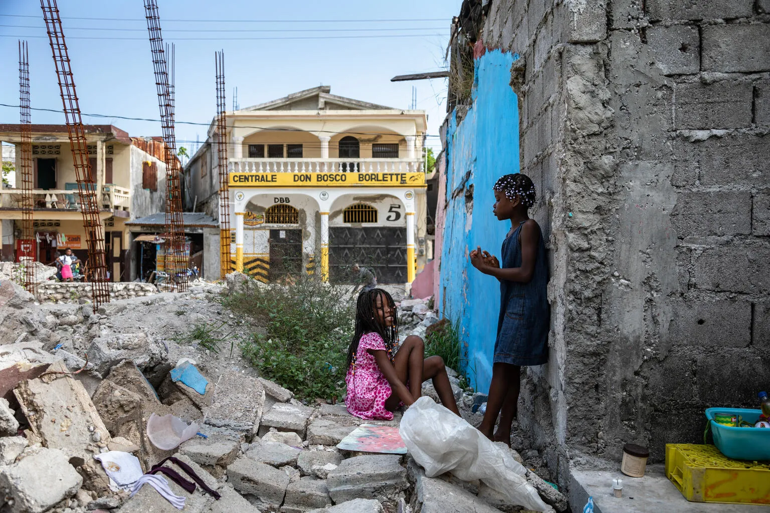 On 18 July 2022 in Les Cayes, Haiti, children play in the rubble of homes destroyed in the 2021 earthquake. The girl in blue lives nearby with her mother, Yolande Felix, and younger sister, Valentine.
