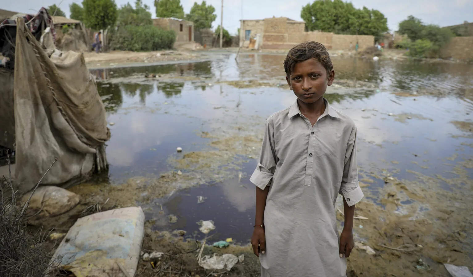 Un enfant regarde dans la caméra, derrière lui se trouvent un champ inondé et des maisons à moitié submergées.