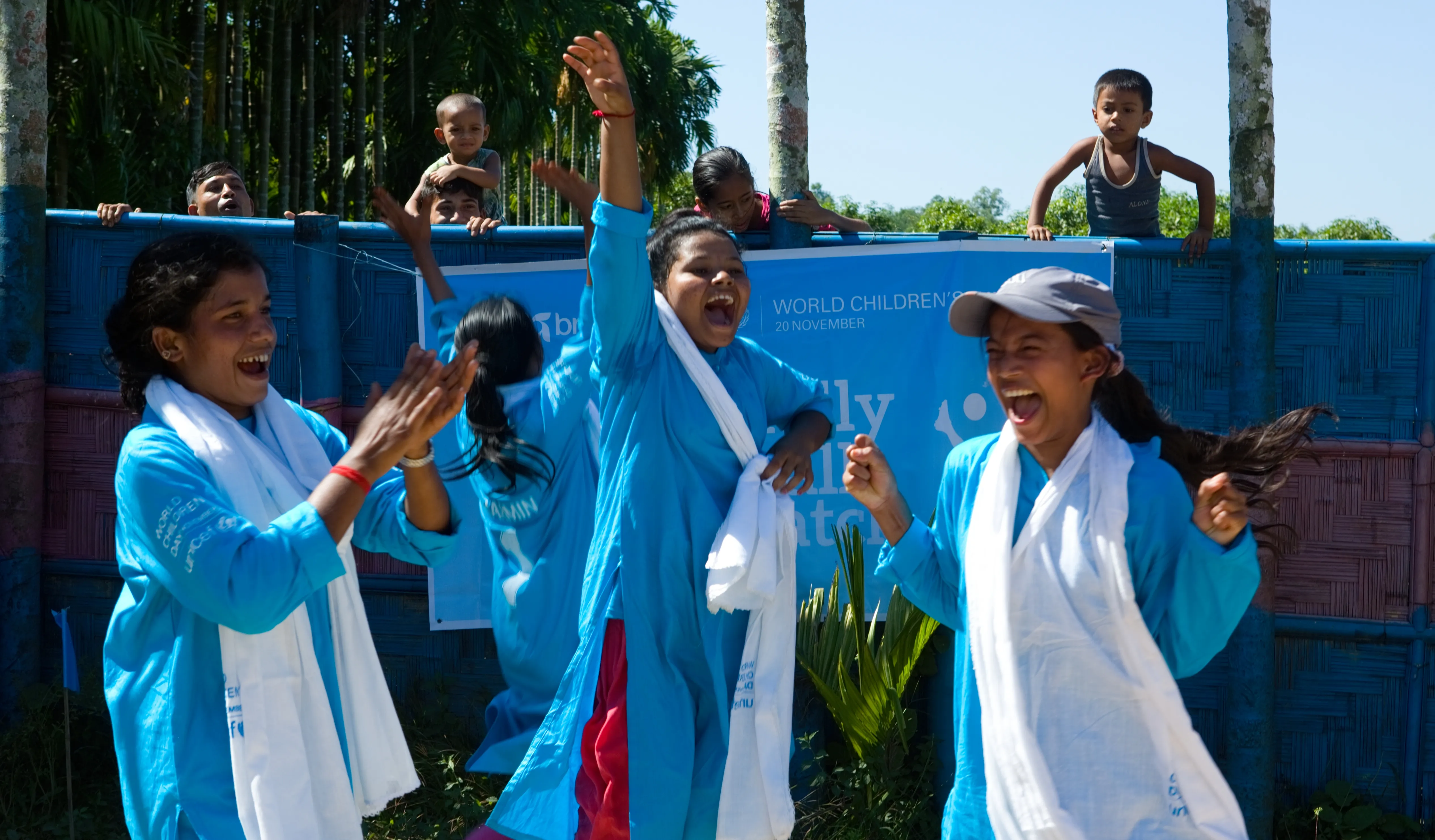 Three girls cheer on the sidelines of a soccer game in Bangladesh. 