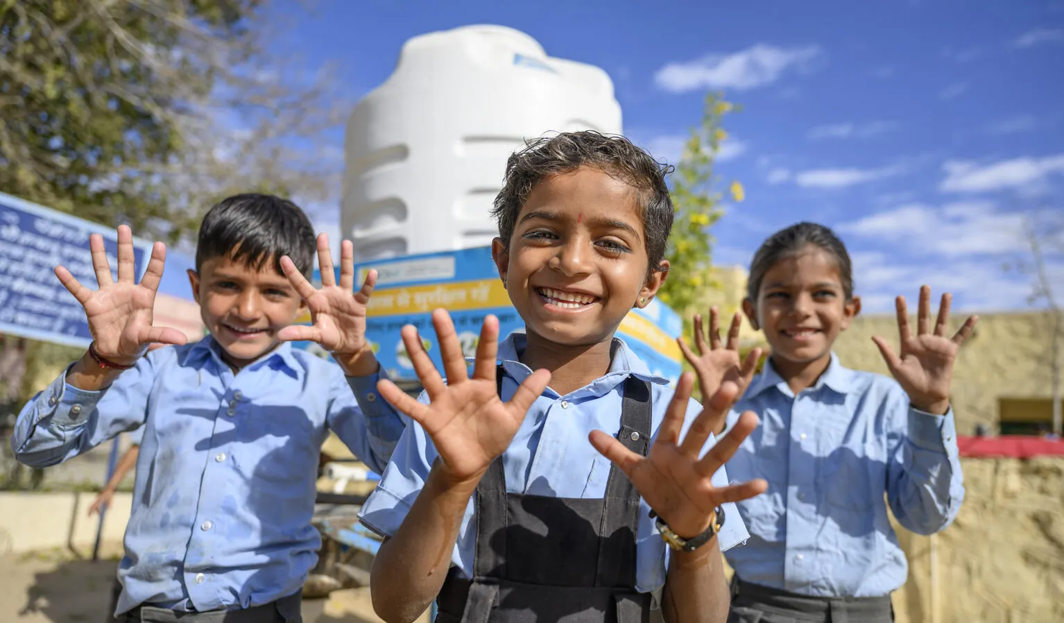 Trois enfants sourient à l’objectif en montrant leurs mains lavées.