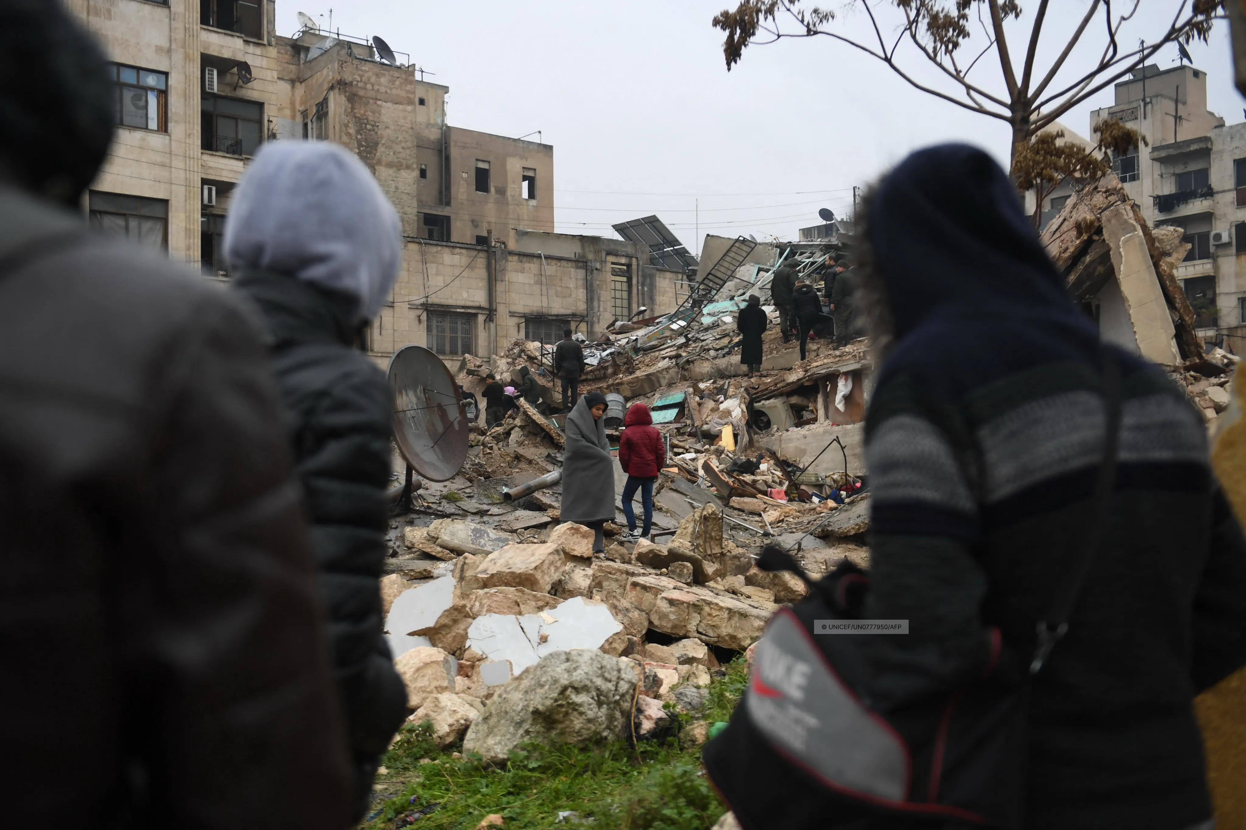 People gather around collapsed buildings as rescue teams look for survivors following an earthquake in the Syrian city of Aleppo