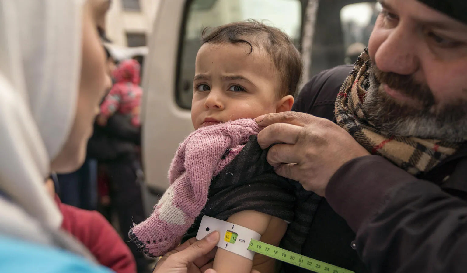 On 10 February 2023, Sondos, two years and eight months, in her father’s arms, is screened for malnutrition by a UNICEF-supported mobile health team worker, using a mid-upper arm circumference (MUAC) tape, in the Alsalheen neighbourhood, Aleppo city, north Syria.