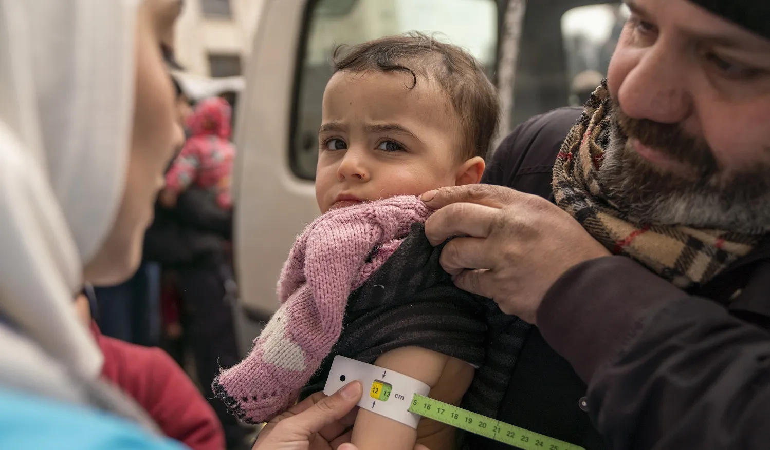 Une membre d’une équipe de santé mobile soutenue par l’UNICEF mesure le bras d’un nourrisson dans les bras de son père à l’aide d’un ruban millimétré afin de procéder au dépistage de la malnutrition.
