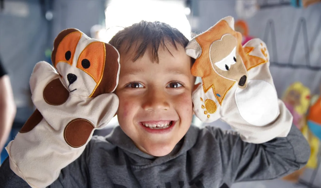 A little boy playing with puppets at a Child Friendly Space in a temporary shelter in Hatay, Türkiye, after two devastating earthquakes hit south-east Türkiye. [© UNICEF/UN0826735/Karacan]