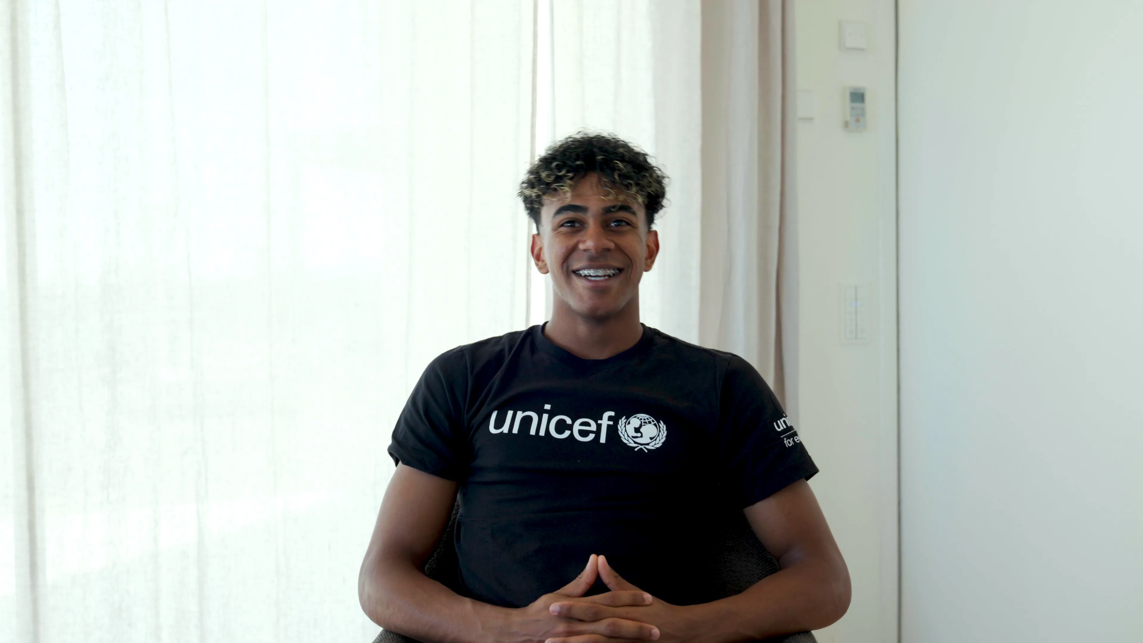 A young man in a black unicef tshirt looking at the camera and smiling. 