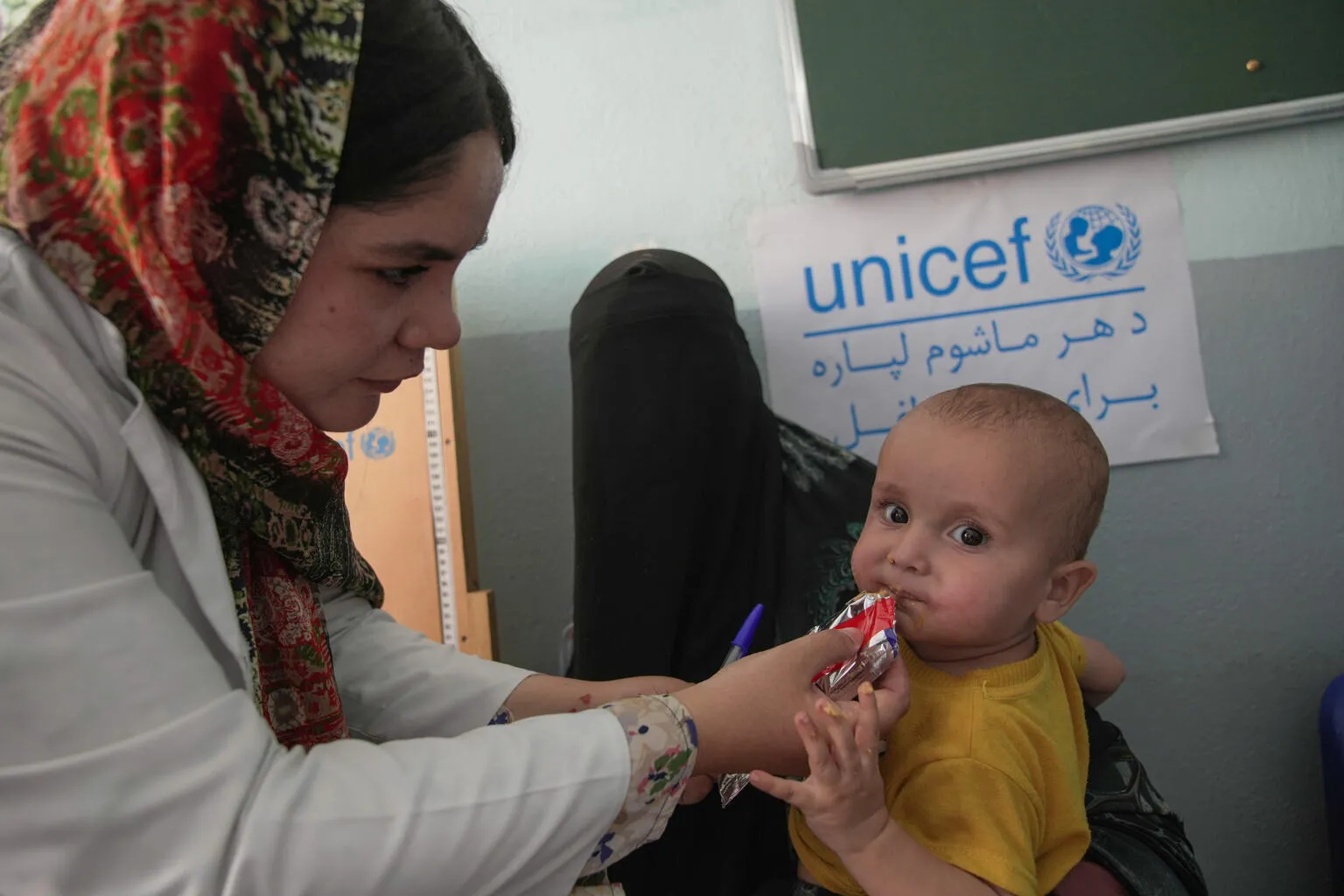 A health worker feeds a child ready-to-eat therepeutic food while his mother holds him 