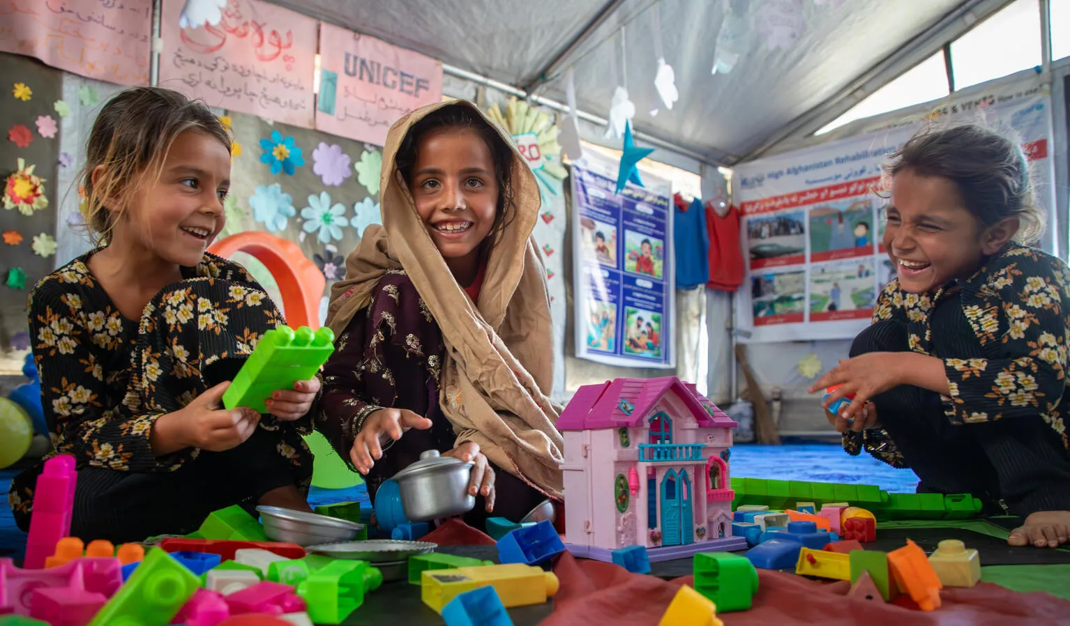 In a tent, three girls laugh and play with toys.