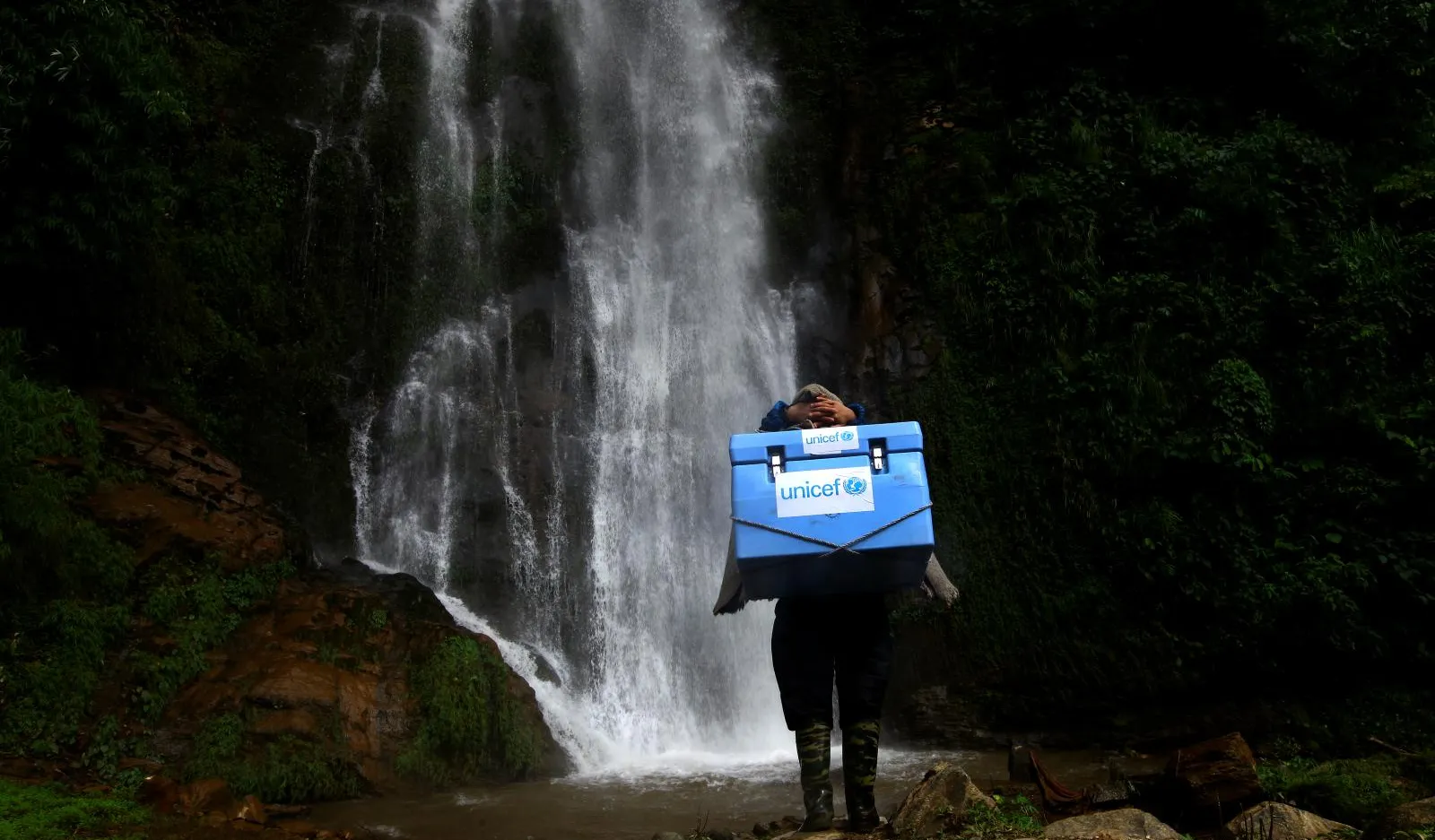 A vaccinator climbs a rocky path.