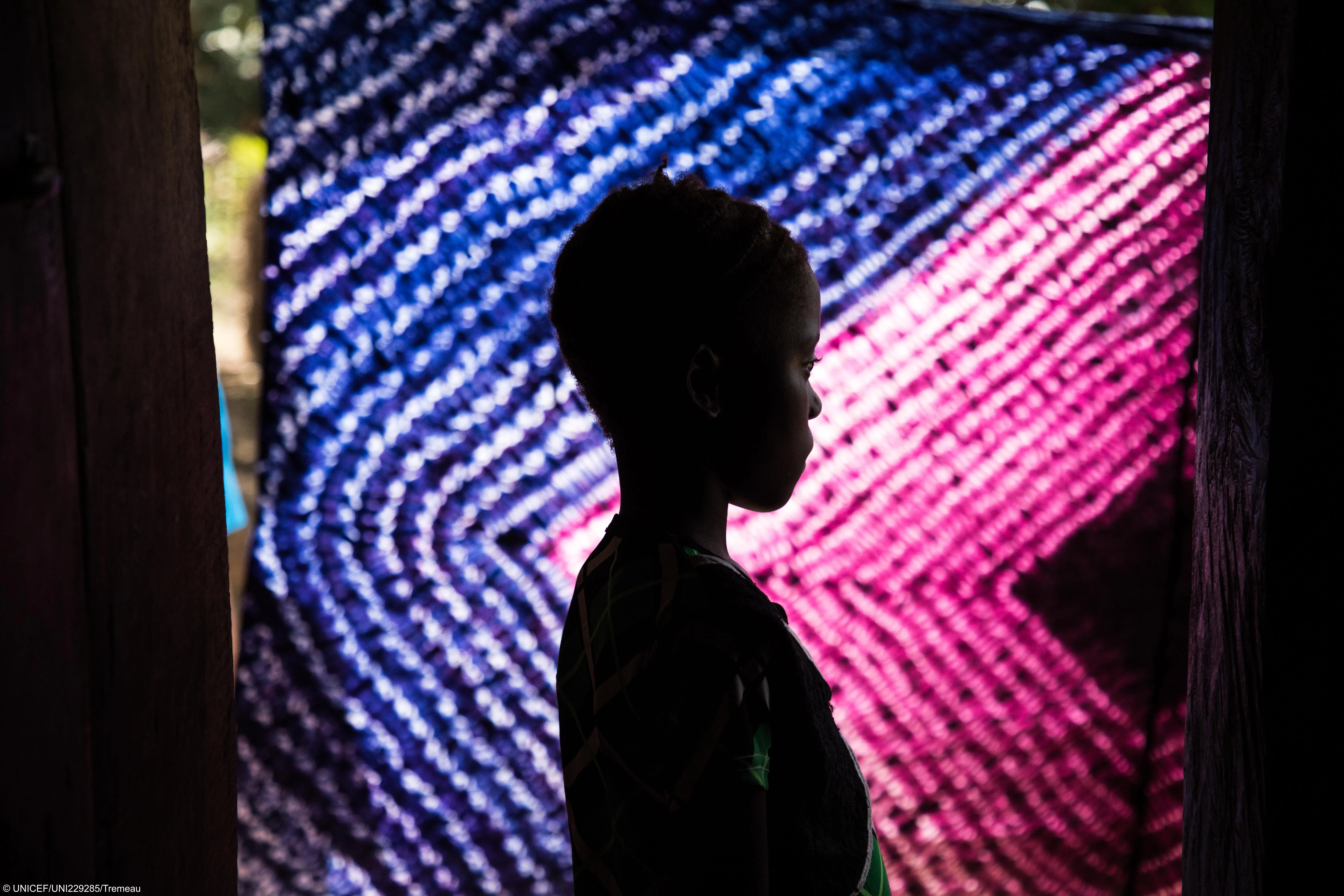 A young girl poses in front of a vibrant, colorful curtain